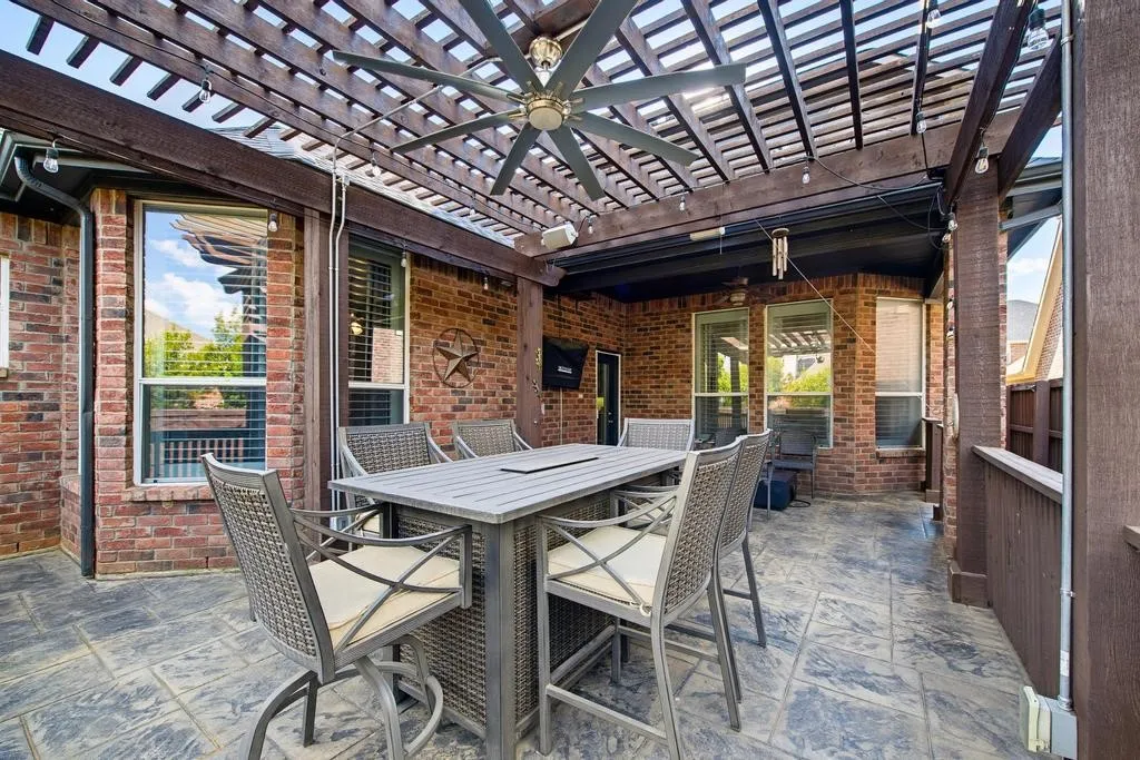 Covered patio featuring a wood pergola and ceiling fan, brick exterior, and stamped concrete flooring