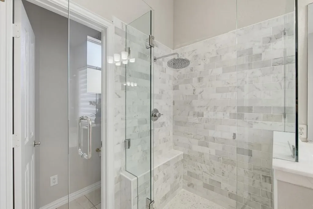 Glass-enclosed shower with subway tile surround, built-in bench, and rain shower head