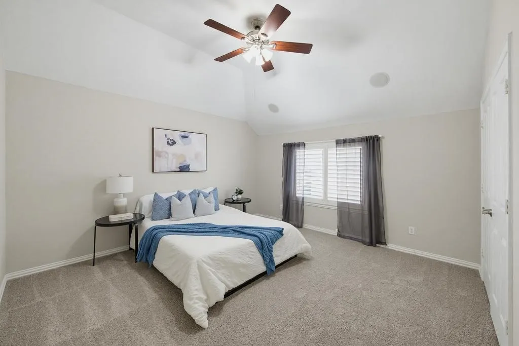 Vaulted ceiling with a ceiling fan, carpeted flooring, and window with plantation shutters