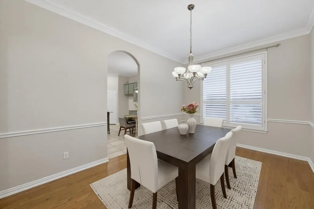 Hardwood flooring, crown molding, chair rail molding, arched doorway, and a chandelier with frosted glass shades