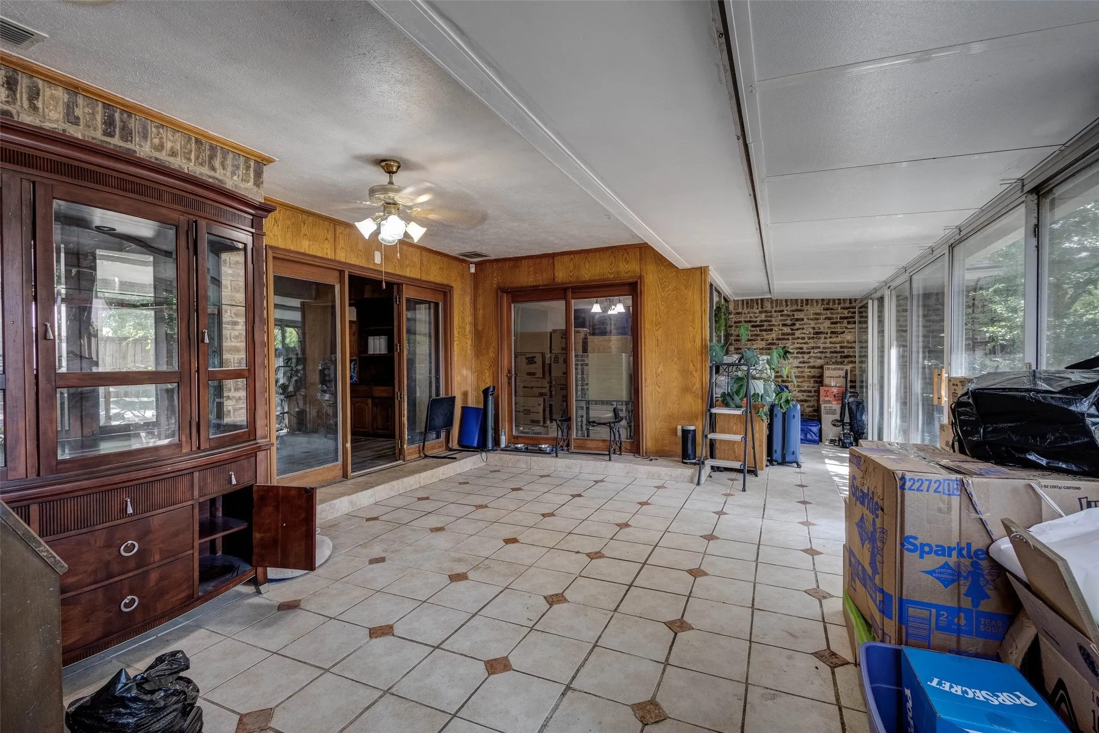 Tiled flooring with accent details, wood paneling, sliding glass doors, brick wall accent, and a ceiling fan