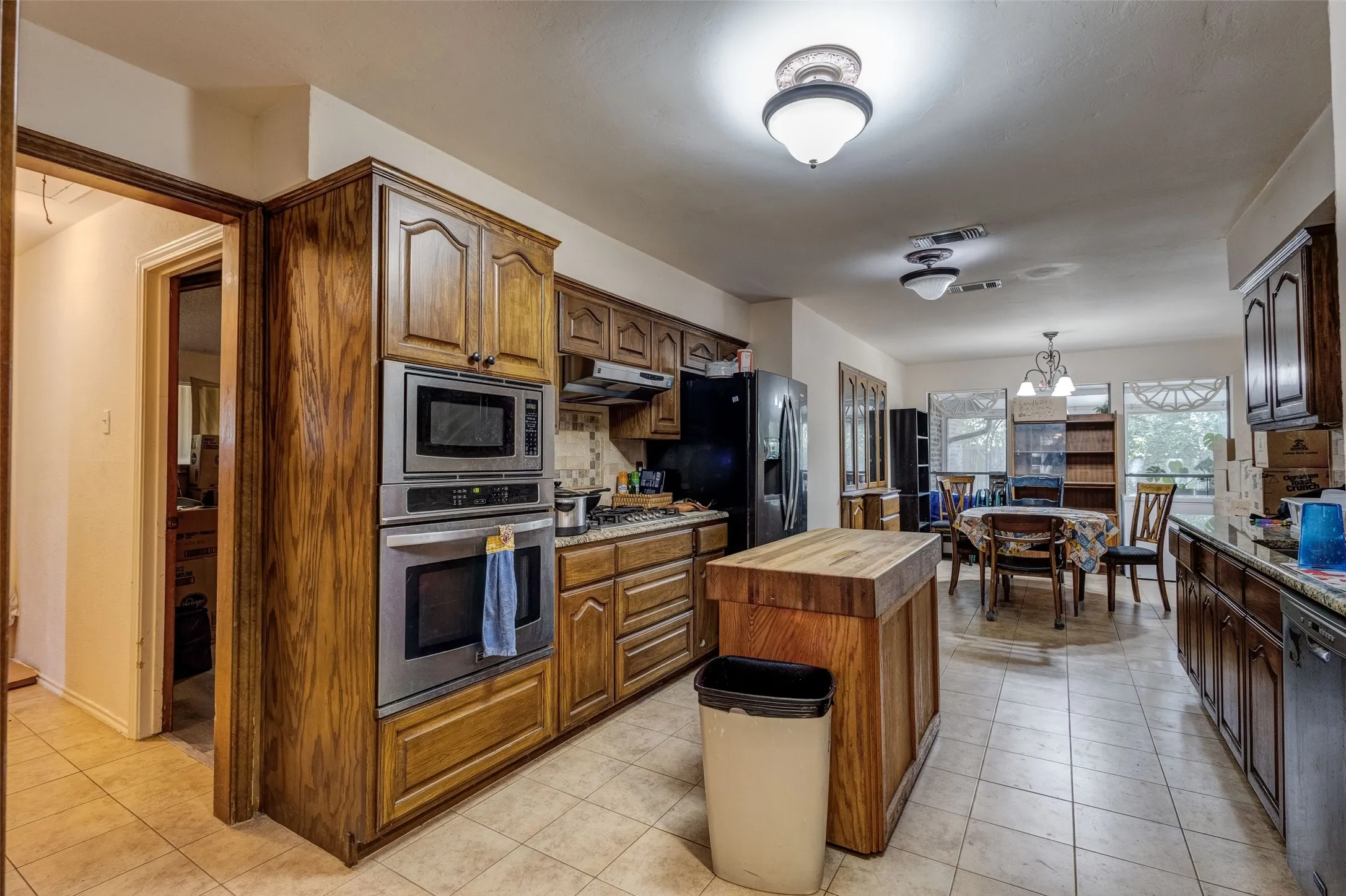 Wood cabinetry, stainless steel double ovens, tile flooring, butcher block island, and recessed lighting