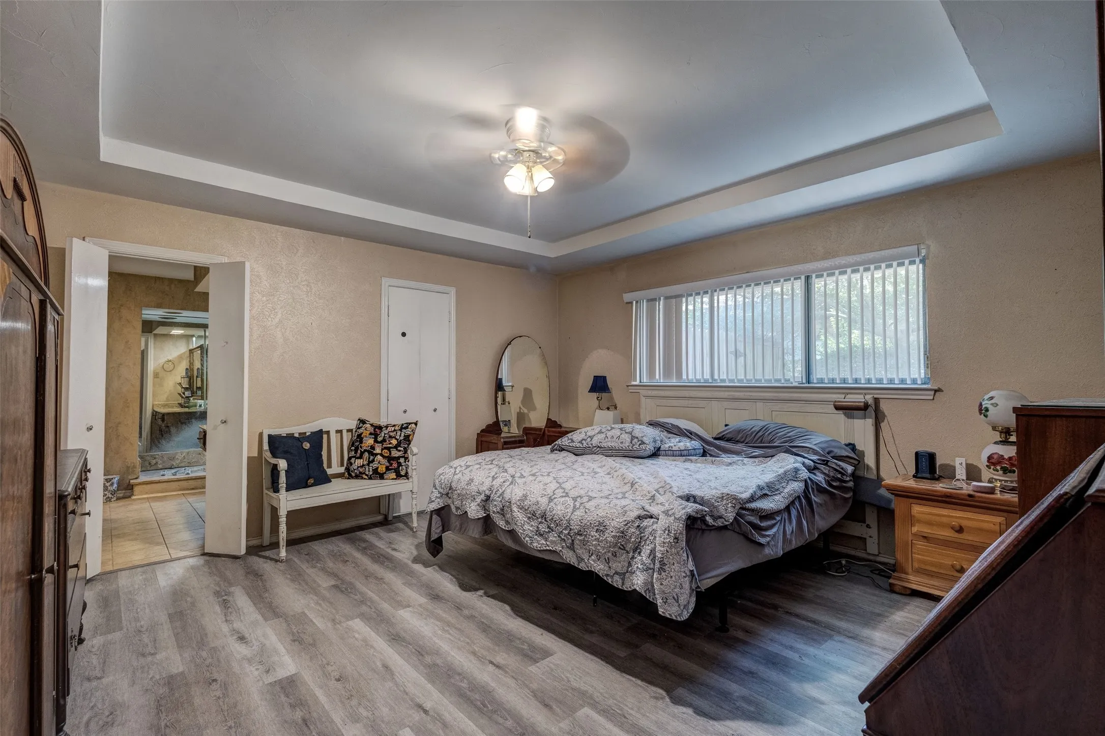 Tray ceiling with a ceiling fan, wood-finish flooring, and a large window with vertical blinds