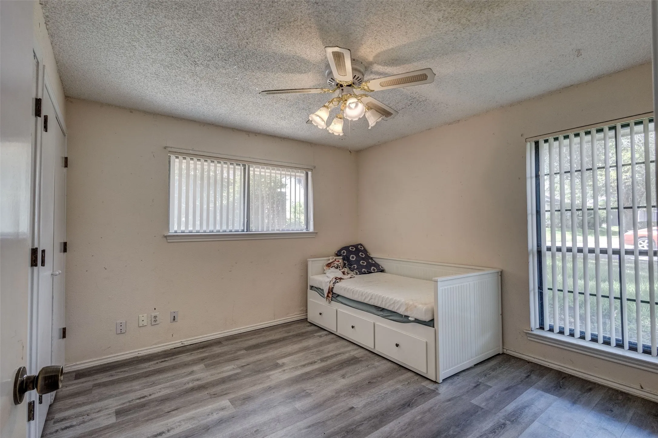 Wood-finish flooring, ceiling fan with light fixture, and two windows with vertical blinds