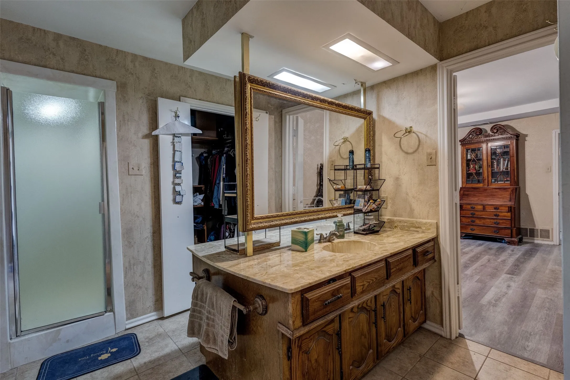 Dual sink vanity with a light-toned countertop, framed mirror, built-in medicine cabinet, and a shower enclosure with frosted glass