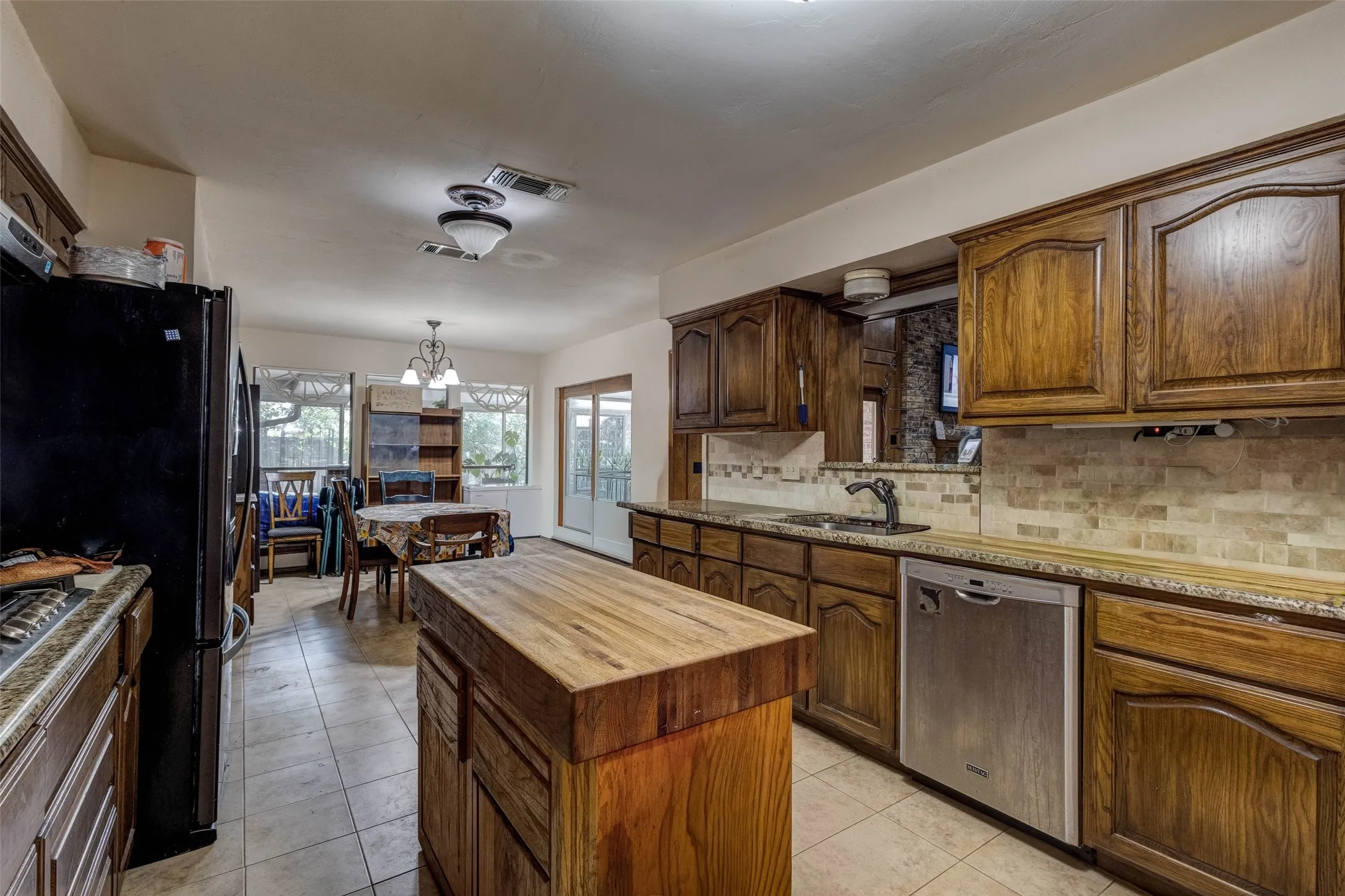 Kitchen featuring wood-finish cabinetry, stainless steel dishwasher, tile flooring, and a butcher block island