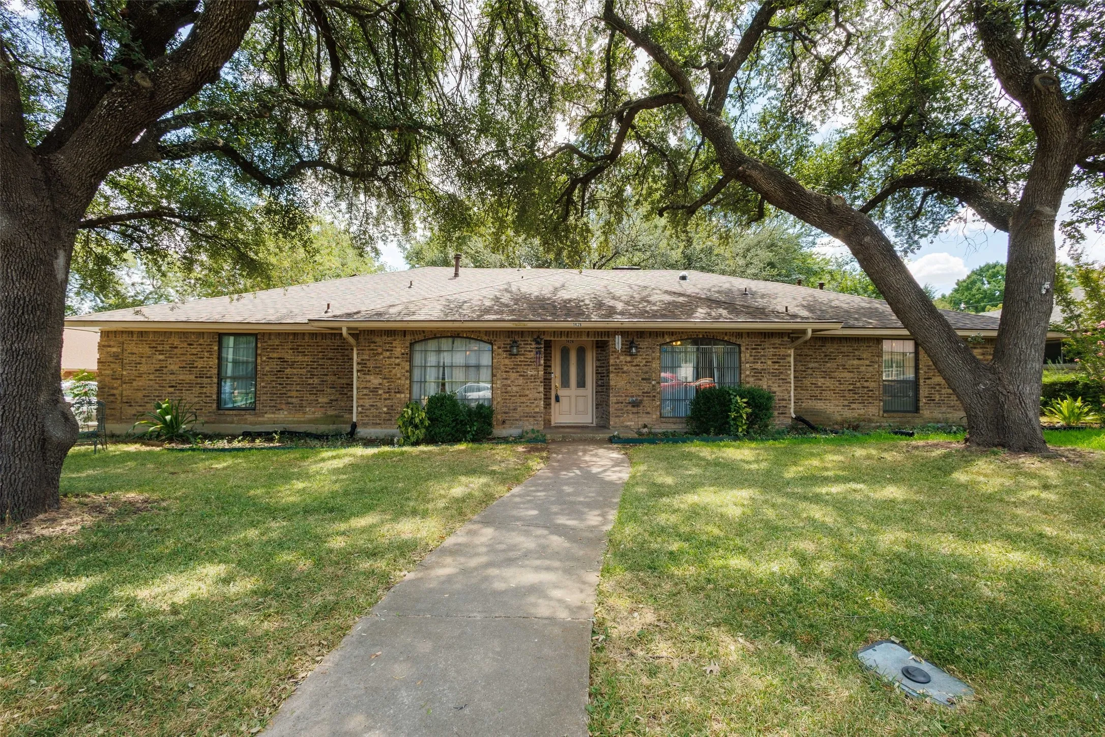 Brick exterior with a shingle roof and mature trees framing the property