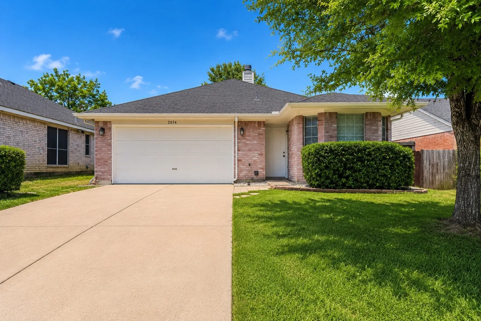 Brick exterior with an attached garage, paved driveway, and mature landscaping