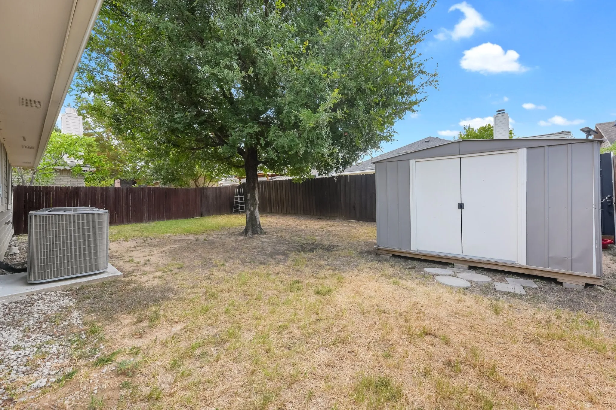 Backyard featuring a mature tree, privacy fencing, and a detached storage shed with double doors