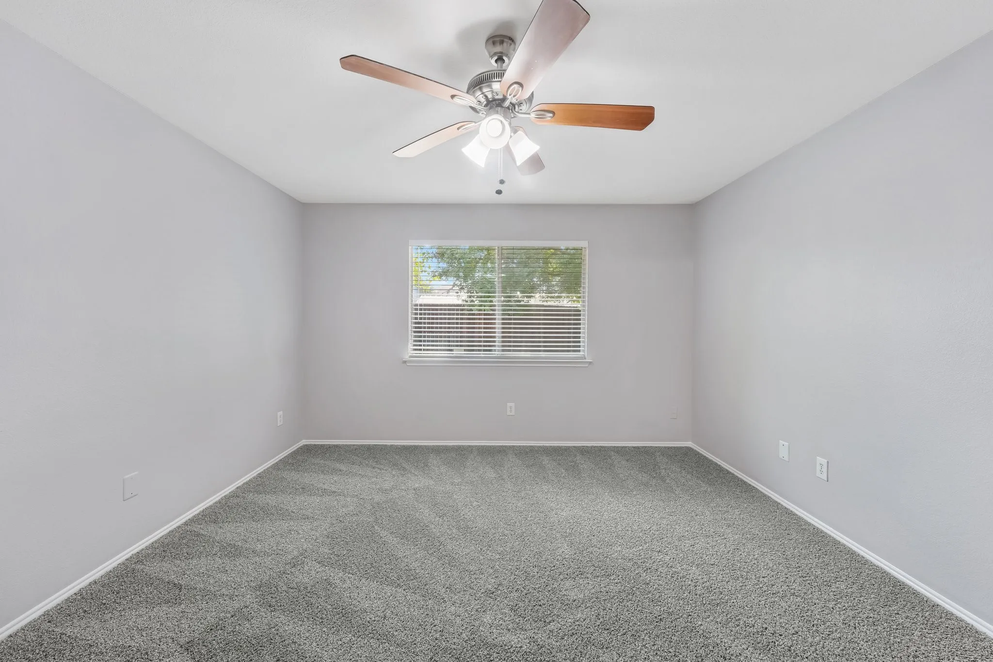 Neutral-toned walls with a window featuring horizontal blinds, gray patterned carpeting, and a ceiling fan with integrated lighting