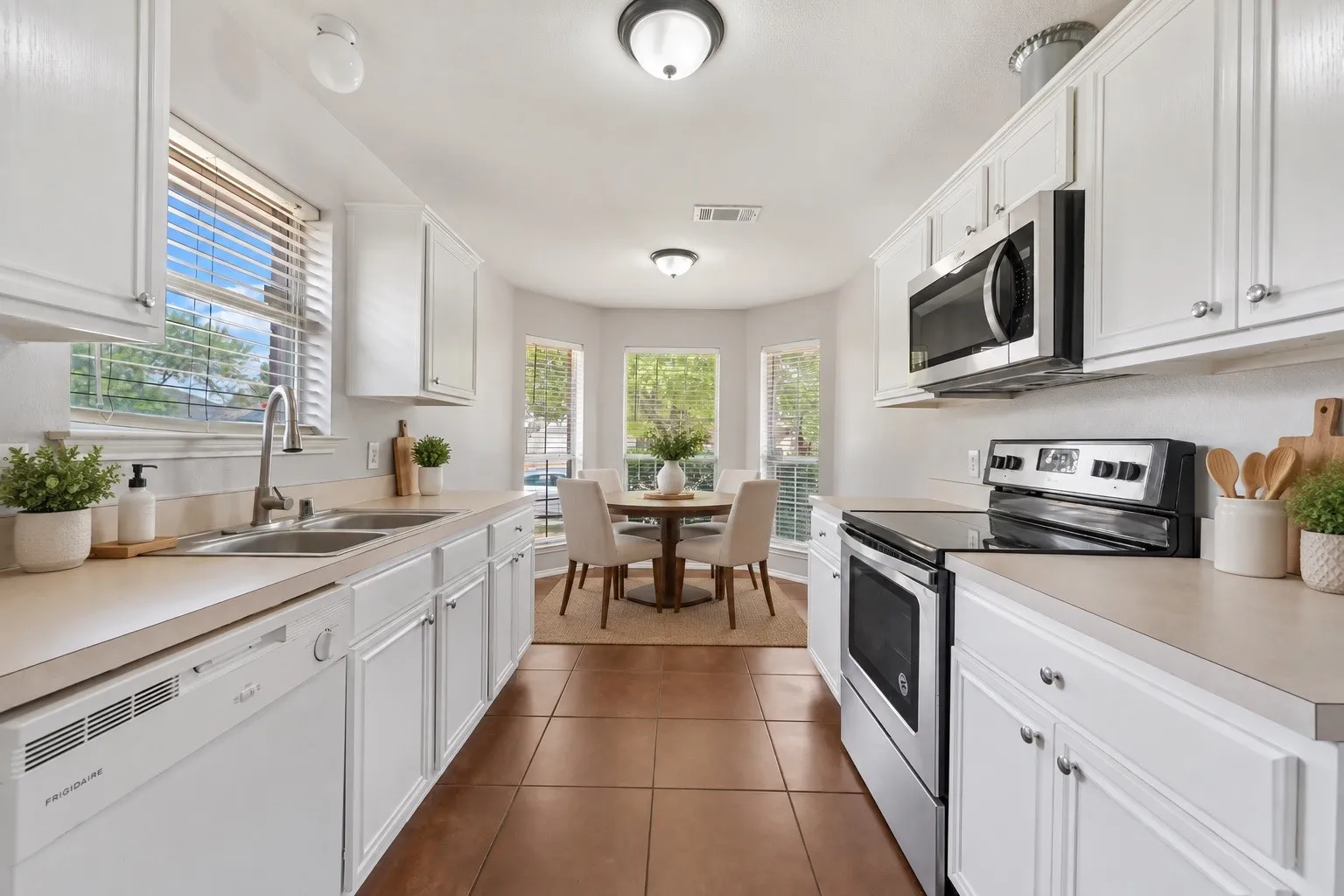 White cabinetry with polished hardware, dual basin stainless steel sink, integrated dishwasher, stainless steel over-the-range microwave, and a four-burner electric range