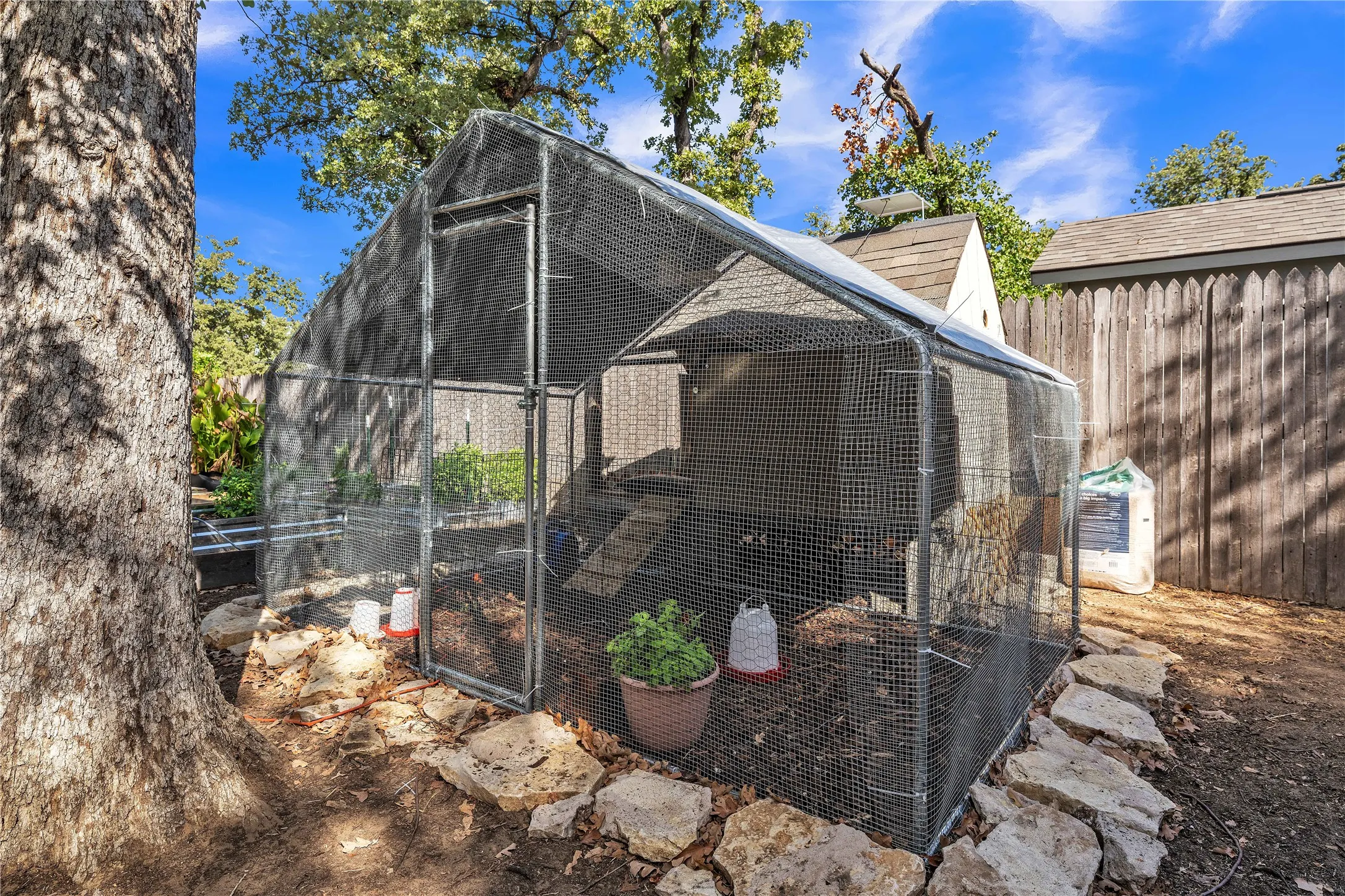 Enclosed animal run featuring wire mesh construction, a sloped roof, and a stone perimeter