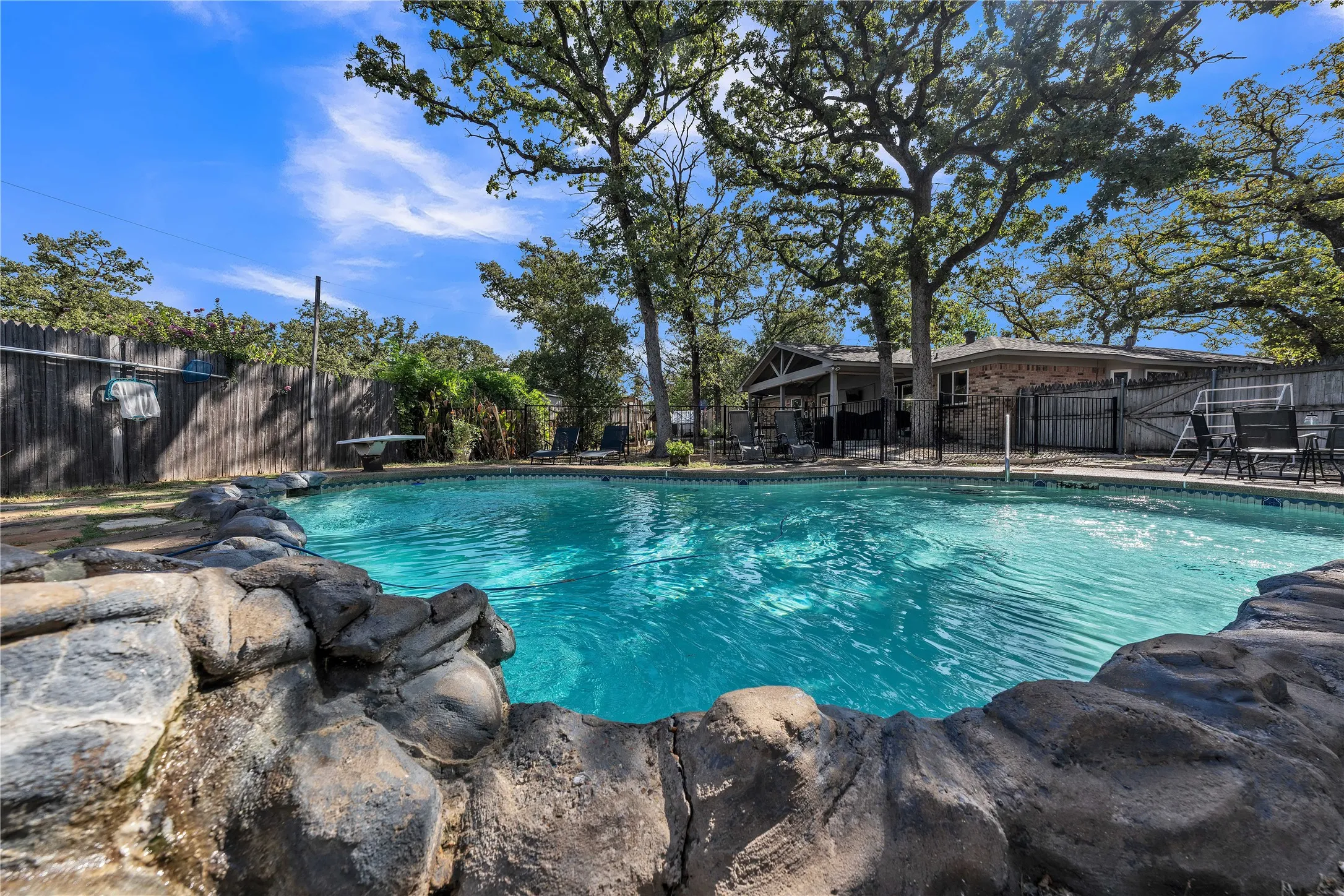 Backyard featuring a built-in swimming pool with rock coping, wood fencing, and mature trees