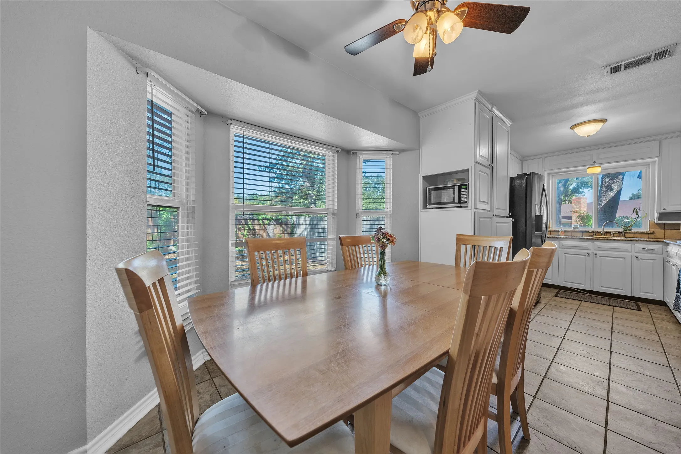 Bay window with multiple panes, kitchen with white cabinetry, built-in microwave, ceiling fan with light fixture, and tile flooring