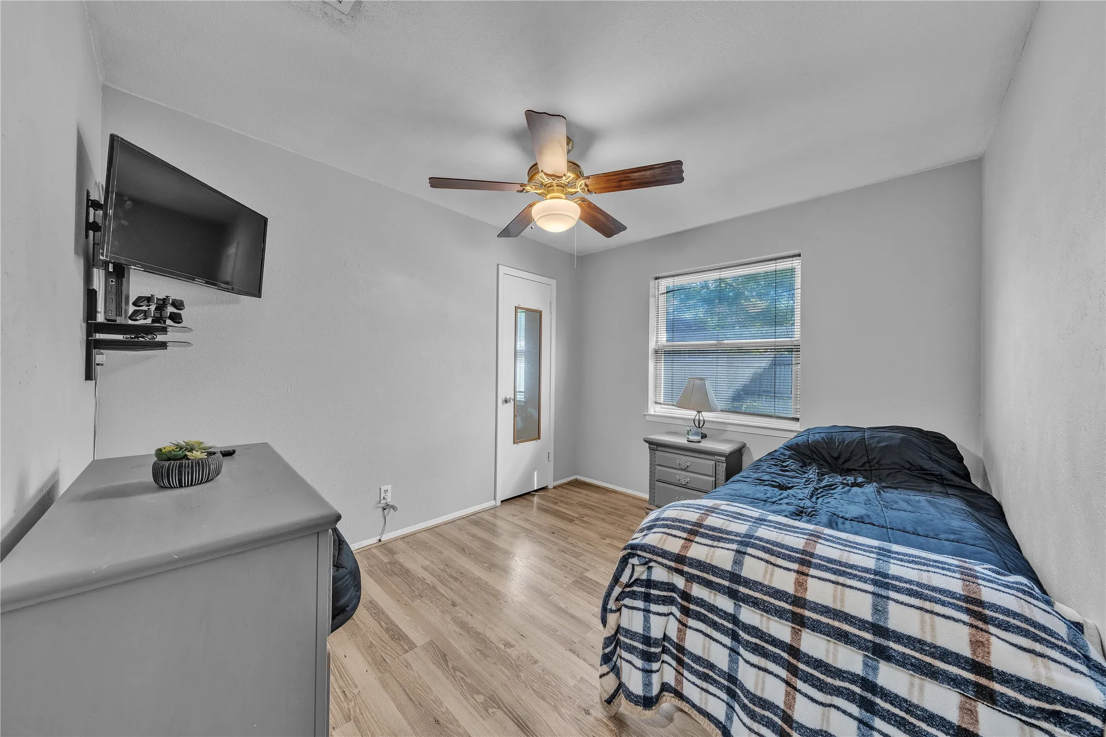 Wood-finish flooring, ceiling fan with light fixture, natural light from a window, and a door with frosted glass panel