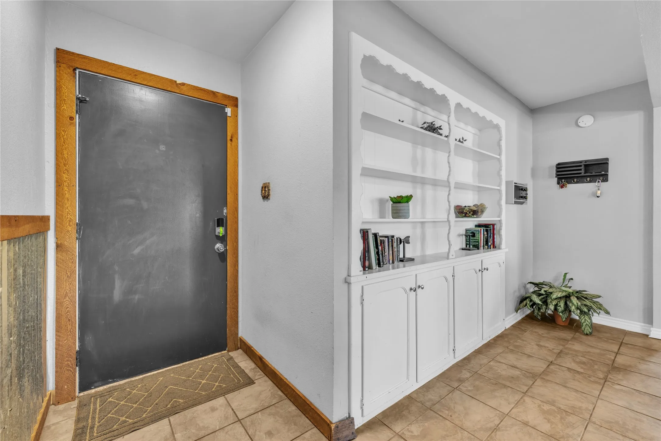 Built-in white shelving and cabinetry, tile flooring, and a dark entry door with wood trim