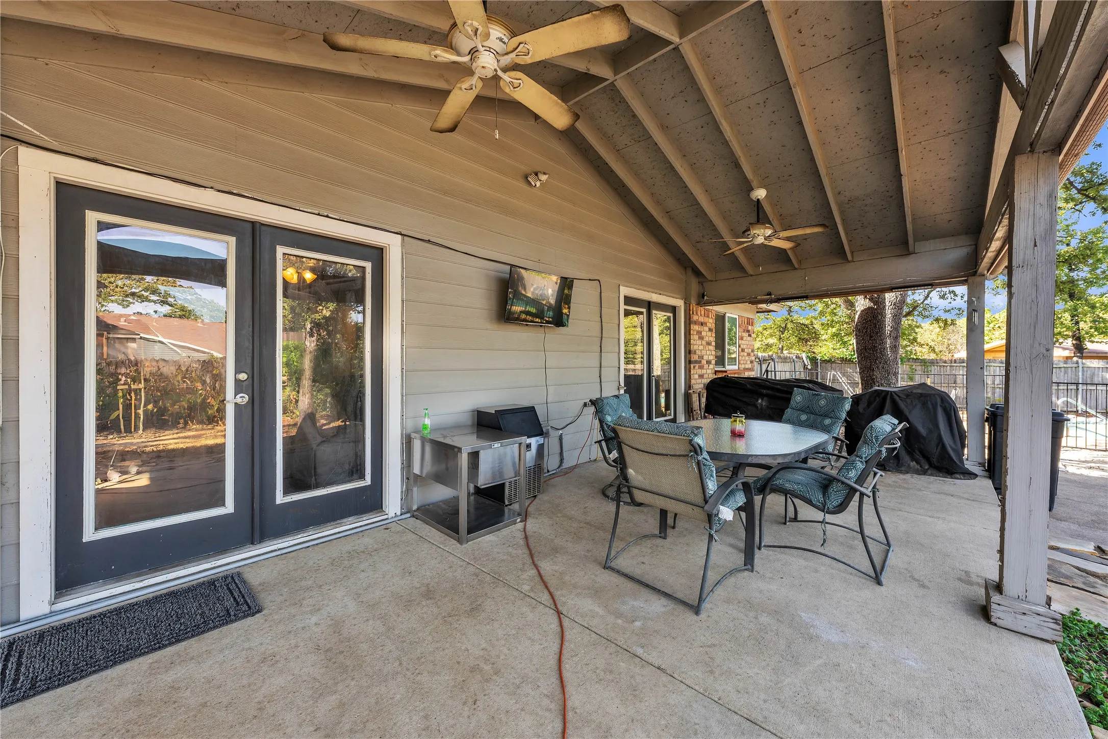 Expansive covered patio featuring a vaulted ceiling with two ceiling fans, dual glass-panel doors, and a concrete surface