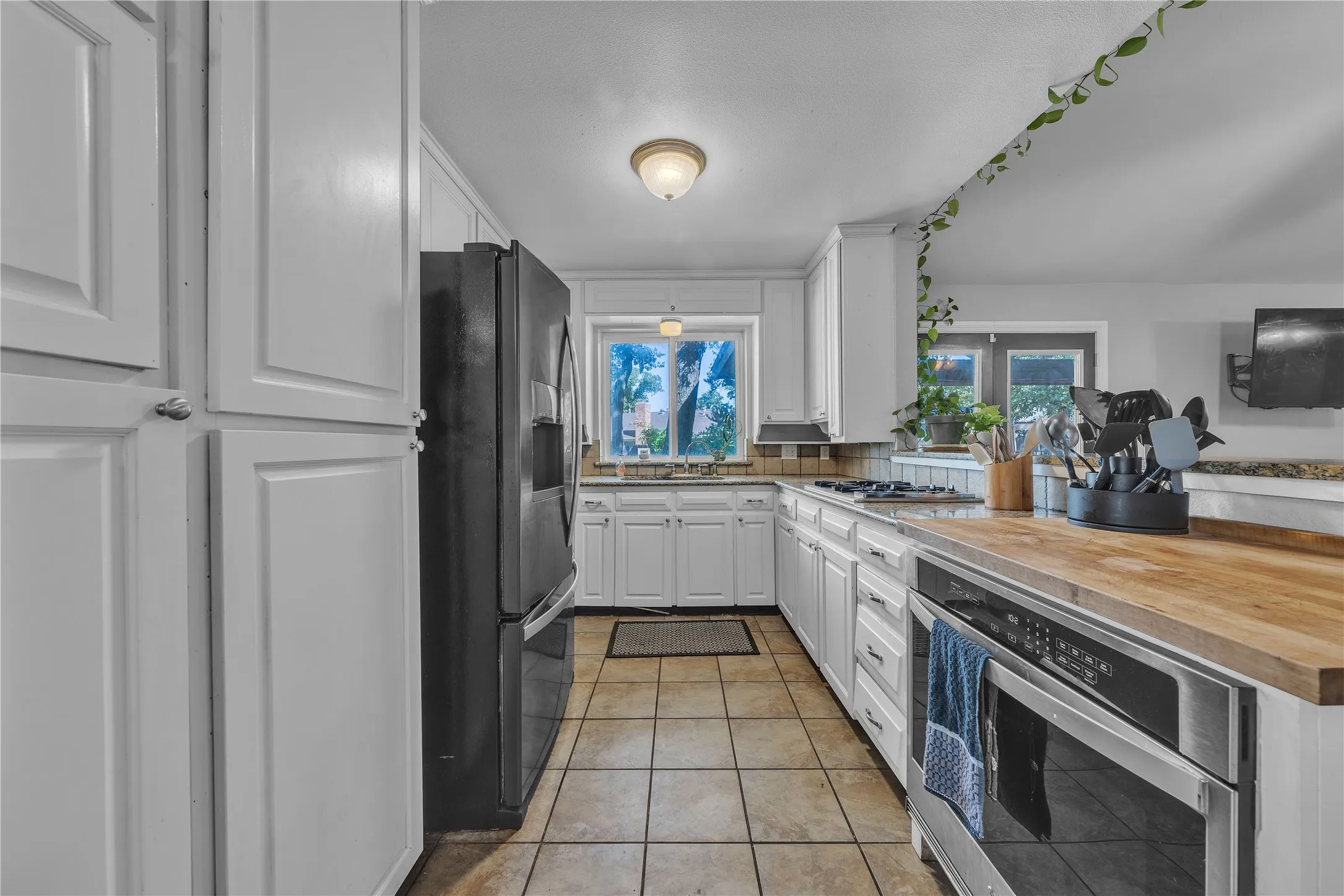 White cabinetry, wood-finish countertops, tile flooring, stainless steel built-in oven, and a gas cooktop