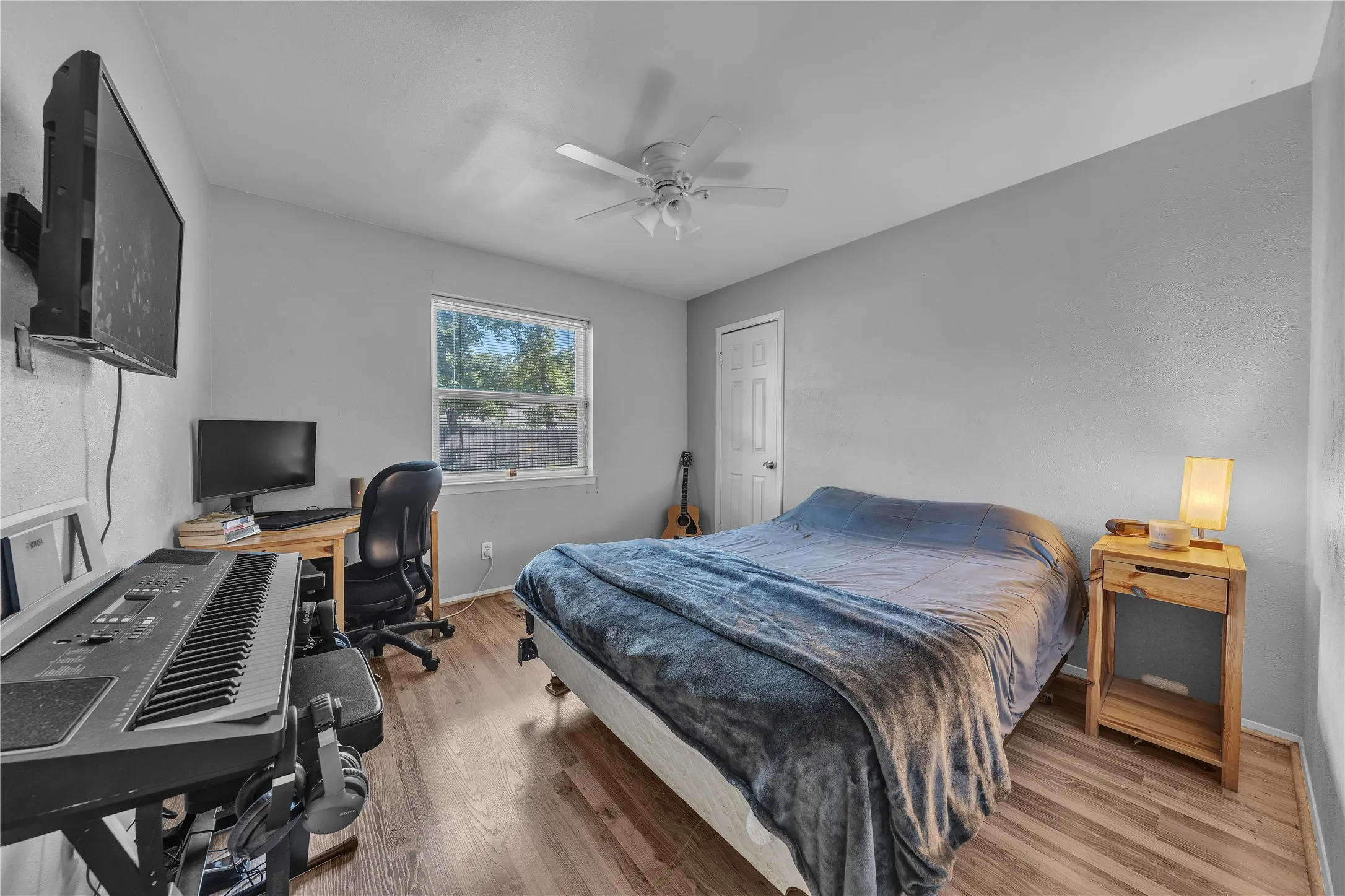 Wood-finish flooring, ceiling fan, single window, and a white interior door