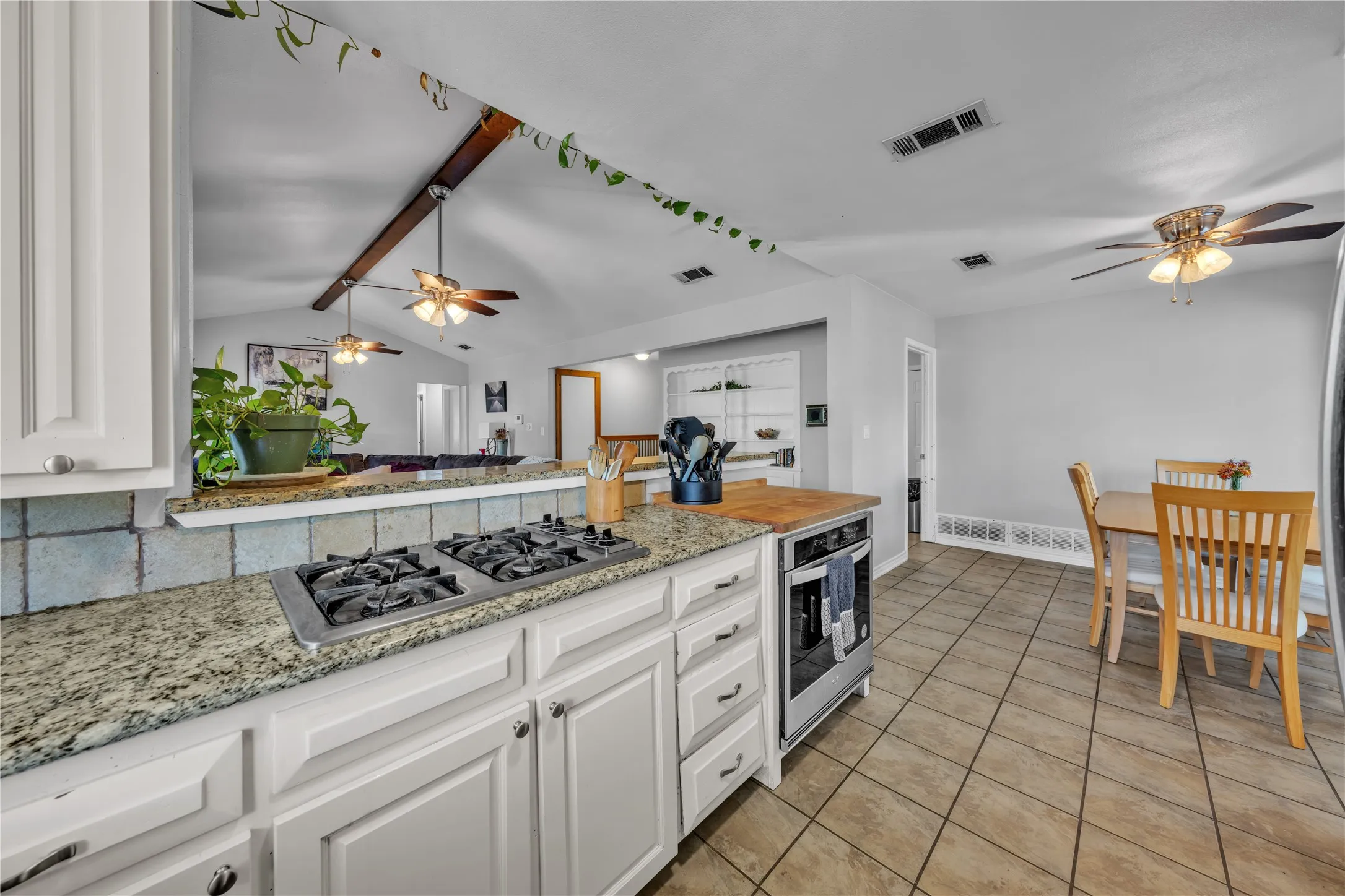 Kitchen featuring white cabinetry, granite countertops, built-in cooktop, tile flooring, and a pass-through bar