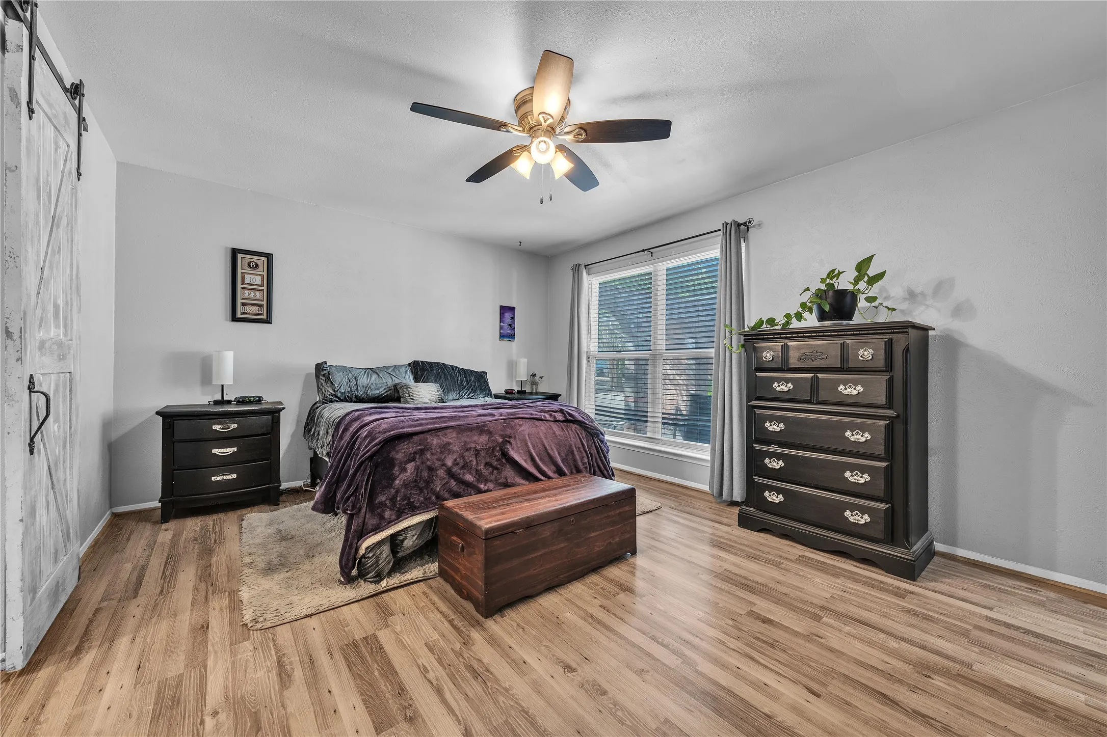 Wood-finish flooring throughout, ceiling fan with integrated lighting, and a window with blinds