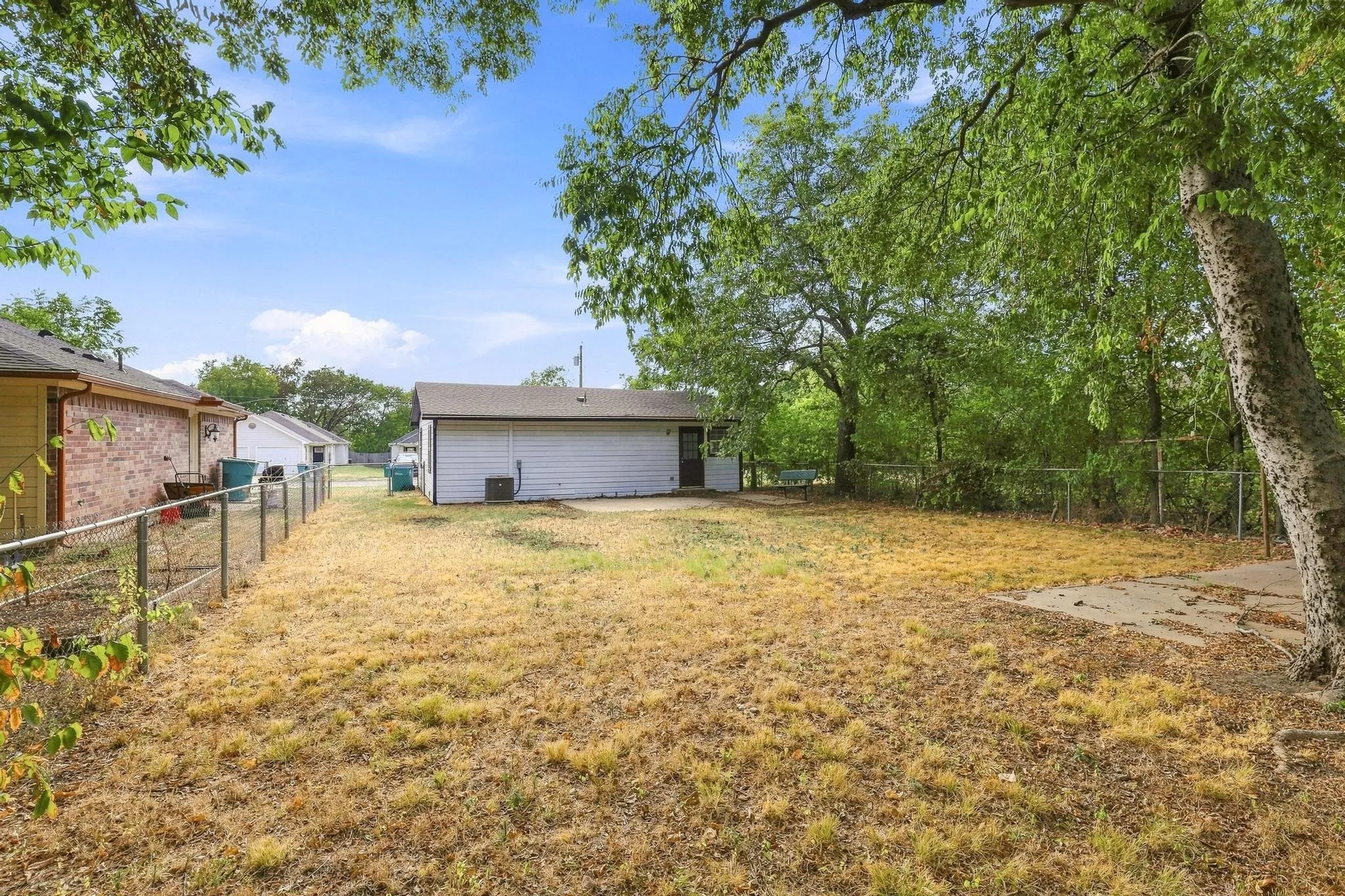 Expansive exterior space featuring a detached structure, partial chain-link fencing, mature trees, and a concrete pad