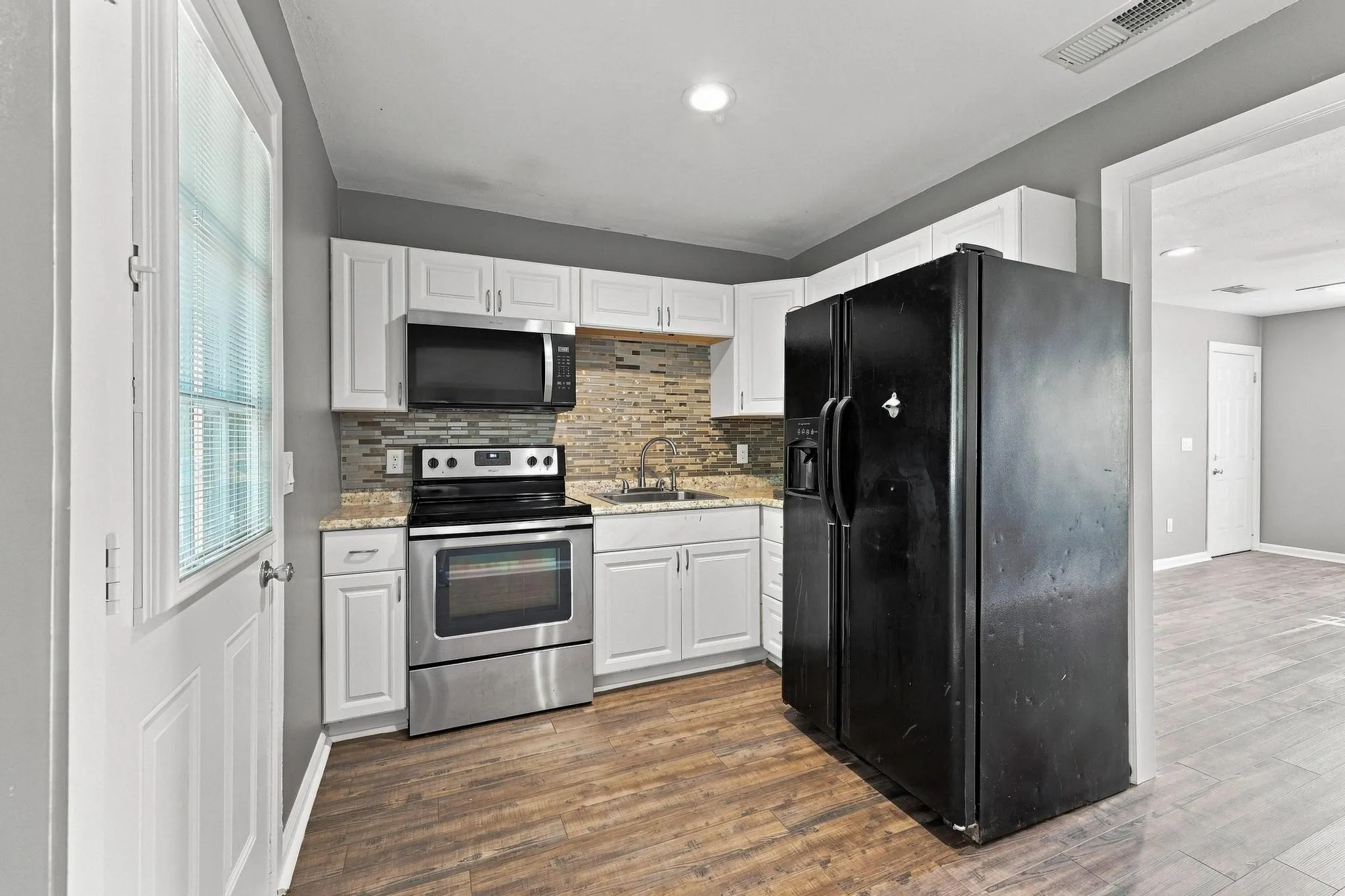Kitchen featuring white cabinetry, wood-finish flooring, stainless steel range, built-in microwave, and tile backsplash