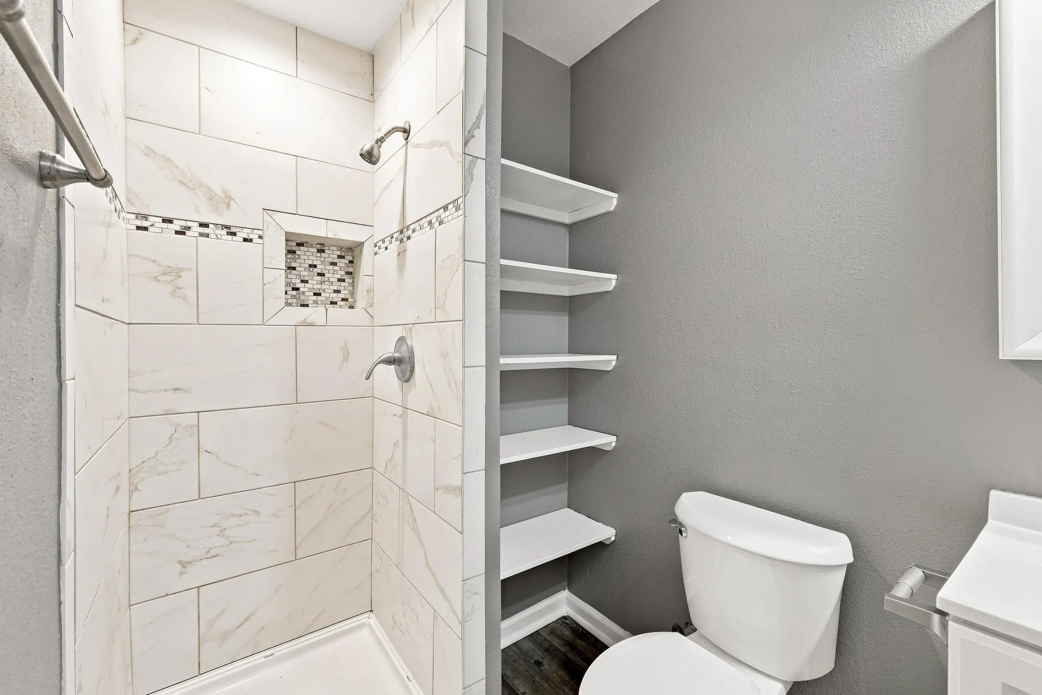 Walk-in shower with large format tile, decorative tile accent band, recessed shower niche, and brushed nickel fixtures