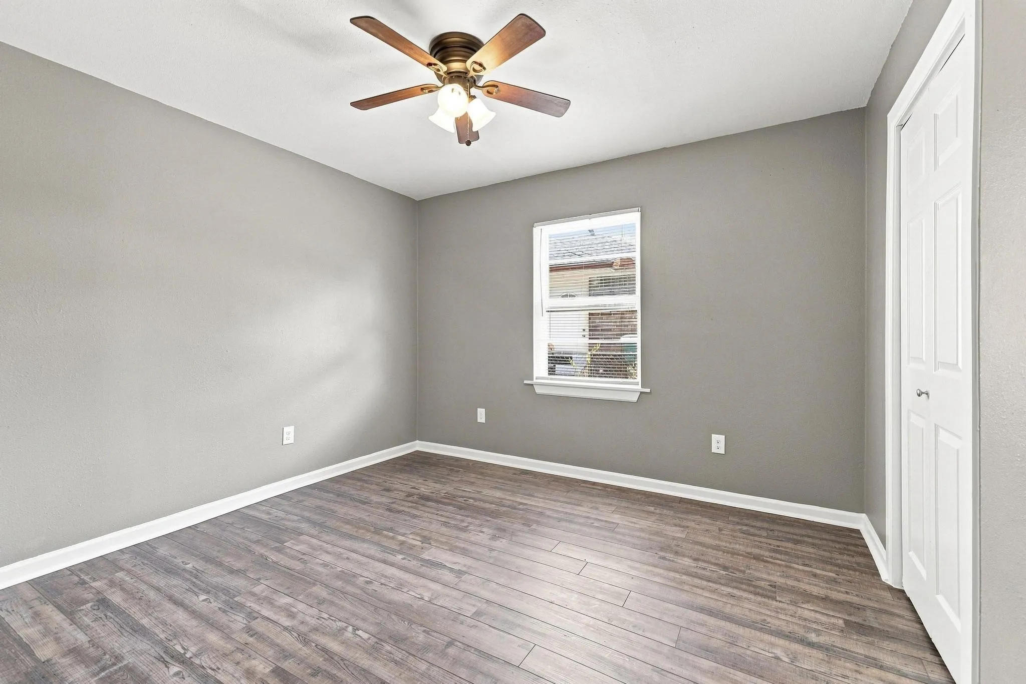 Wood-finish flooring, neutral gray walls, bright white trim, a ceiling fan, and a bi-fold closet door