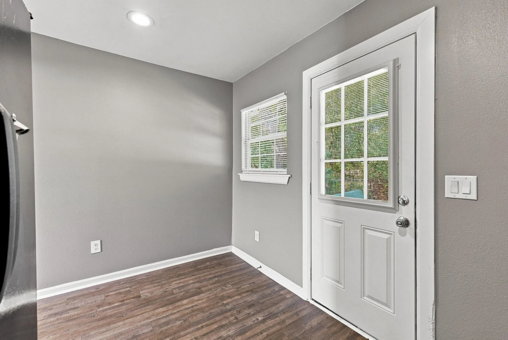 Recessed ceiling lighting, wood-finish flooring, and a white paneled door with divided light glass