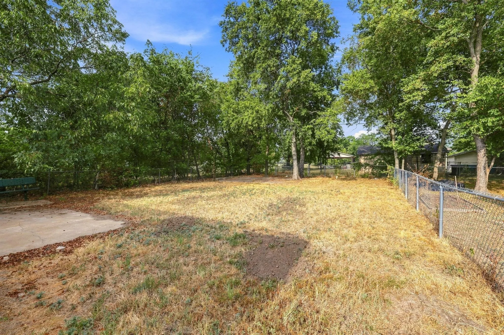 Expansive rear yard featuring a chain-link fence, a concrete patio, and mature trees