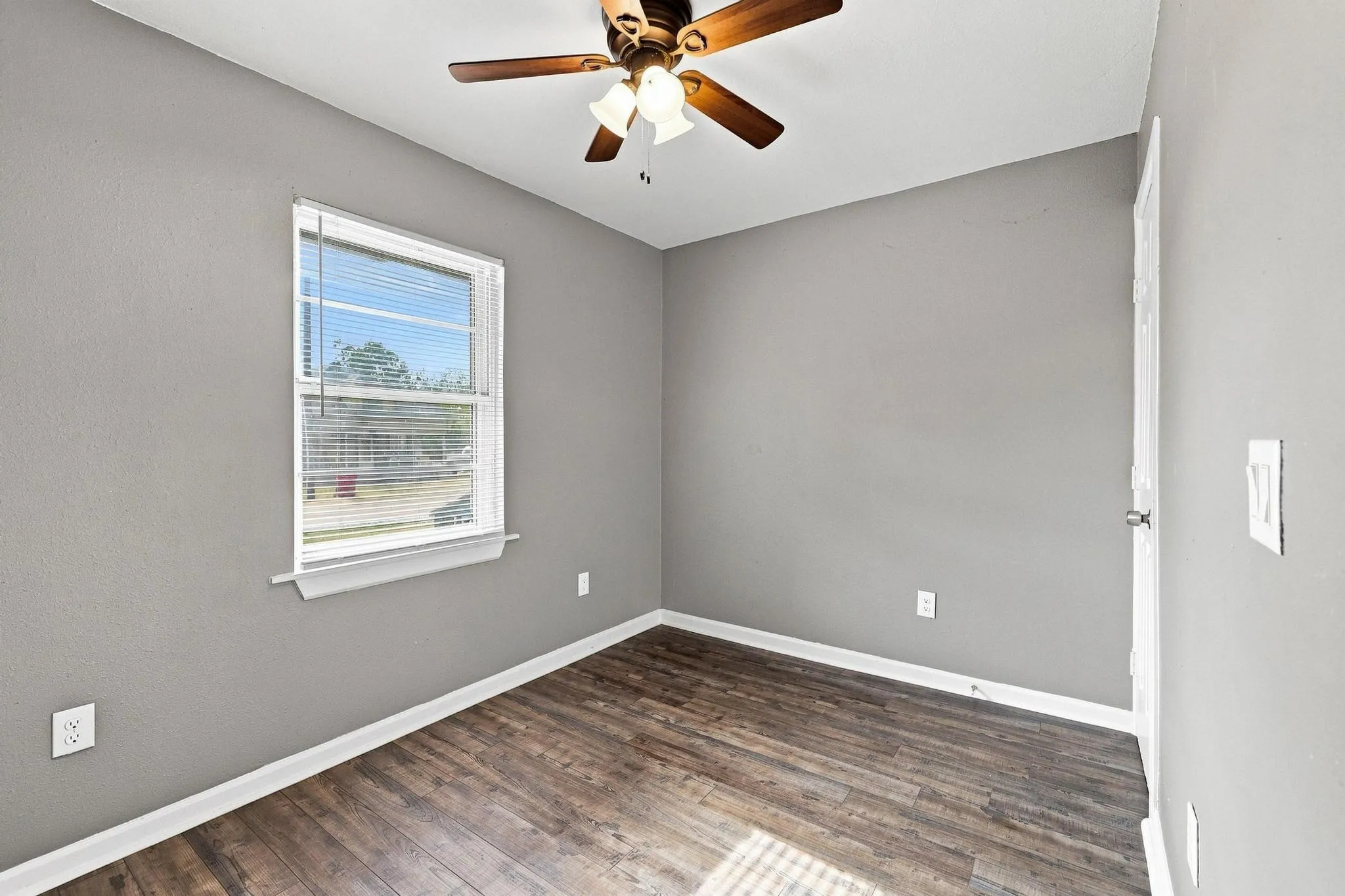 Window with blinds, wood-finish flooring, ceiling fan with light fixture, and neutral wall tones