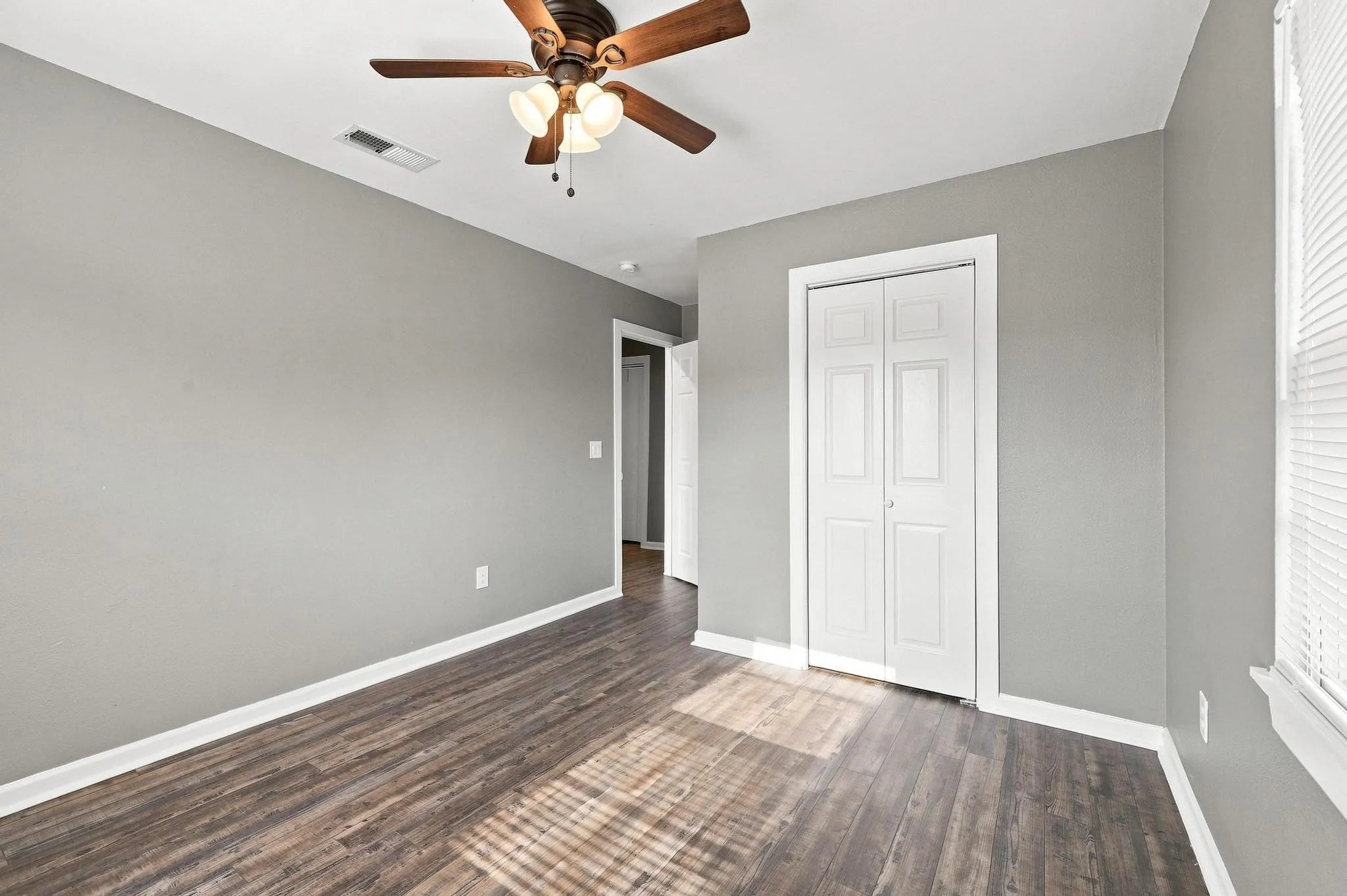 Wood-finish flooring with light gray wall paint, white bi-fold closet doors, and a ceiling fan with light fixture
