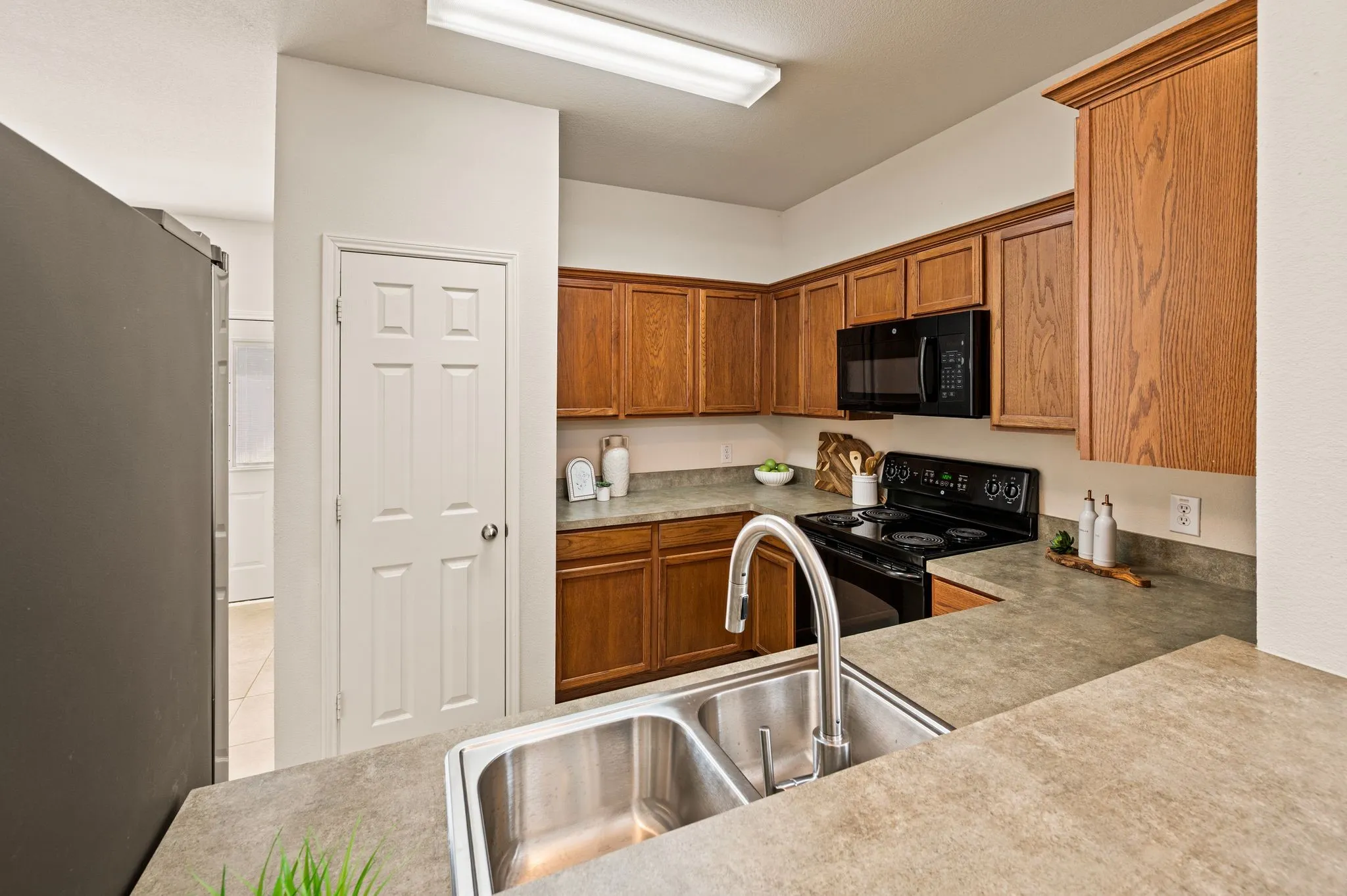 Kitchen featuring wood cabinetry, a dual basin stainless steel sink with a high-arc faucet, and black appliances