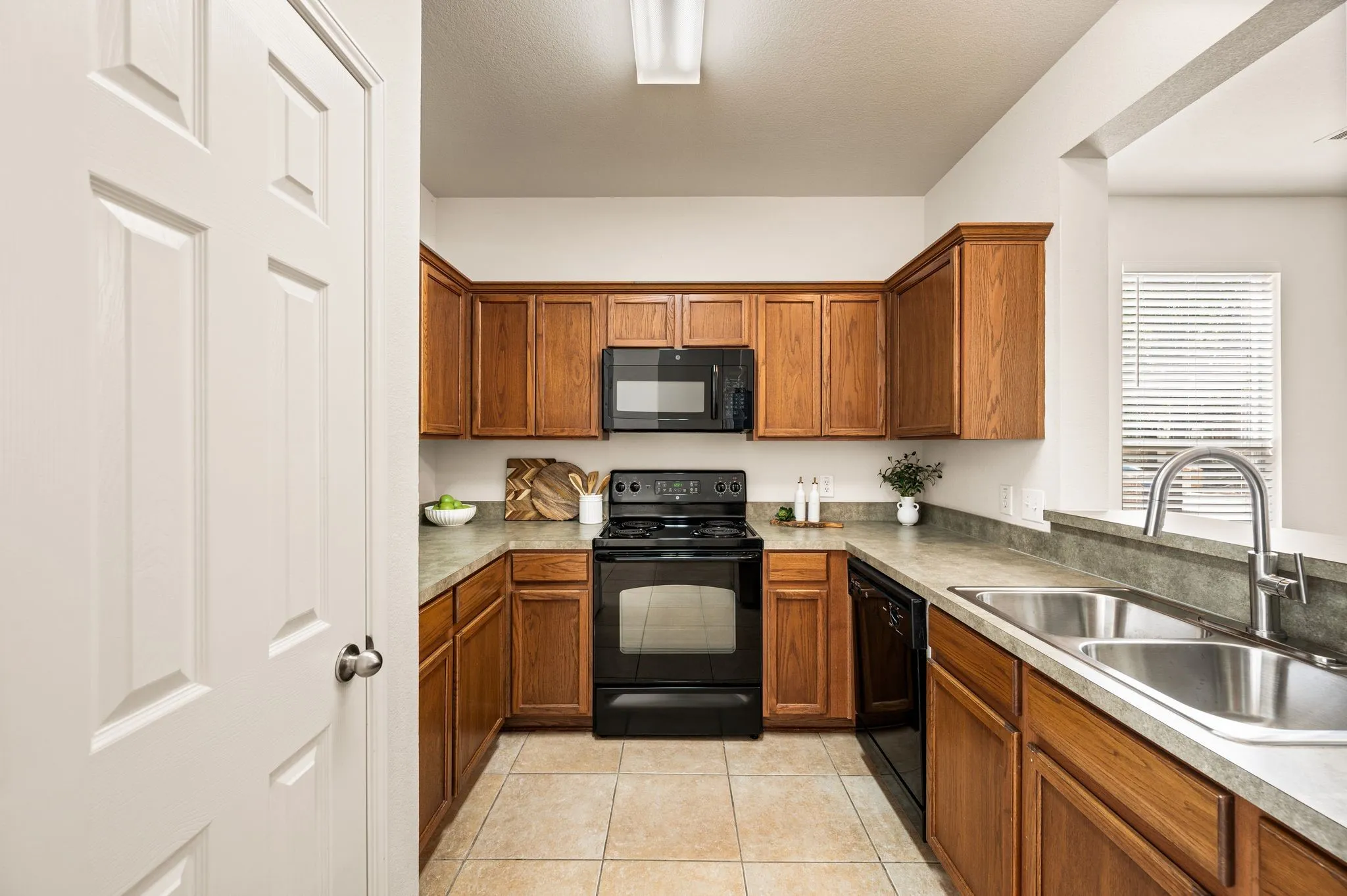U-shaped kitchen featuring wood cabinetry, stone-finish countertops, black appliances, a double basin stainless steel sink, and tile flooring