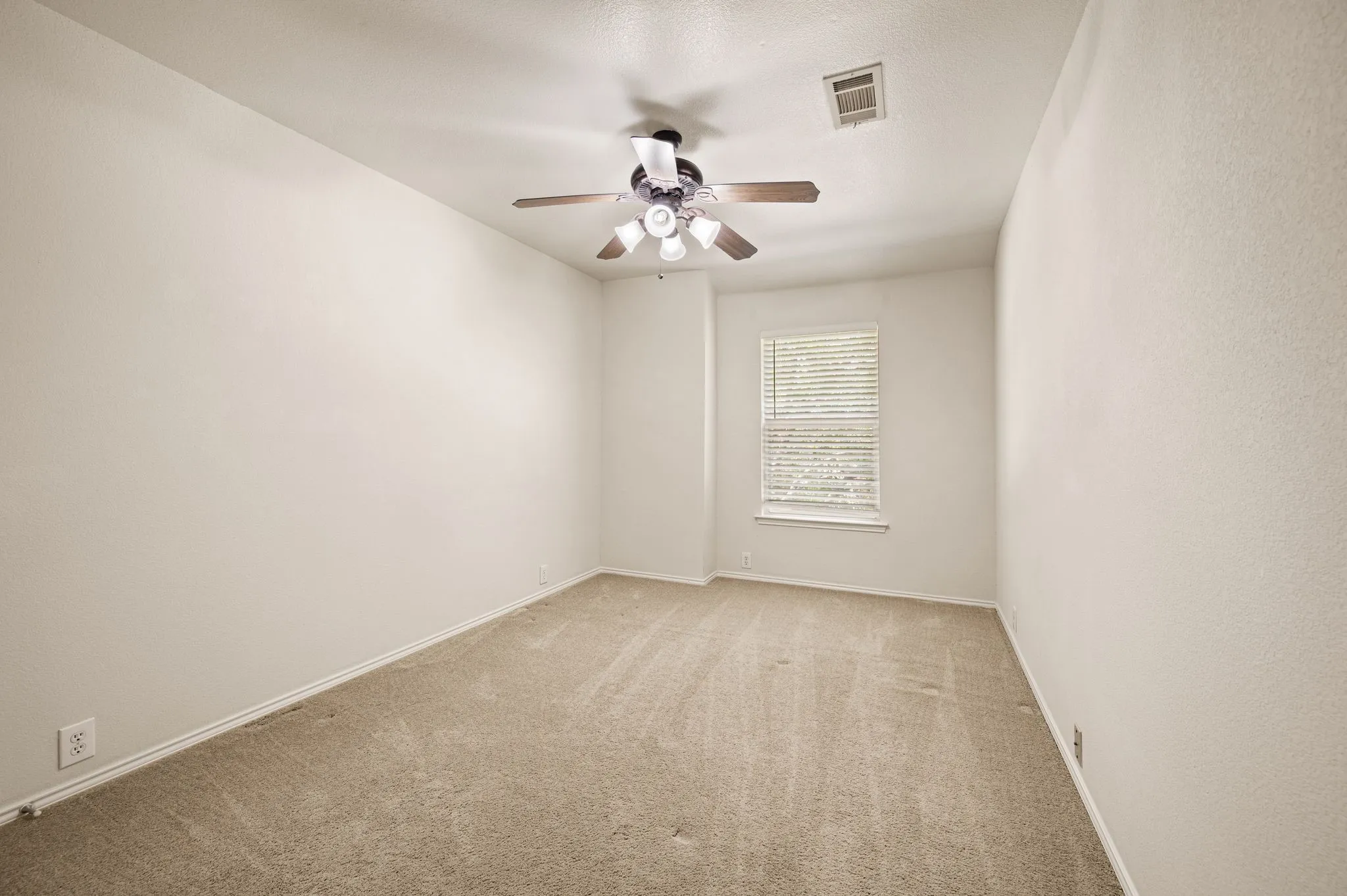 Neutral tone wall paint, carpet flooring, window with blinds, and a ceiling fan with integrated lighting