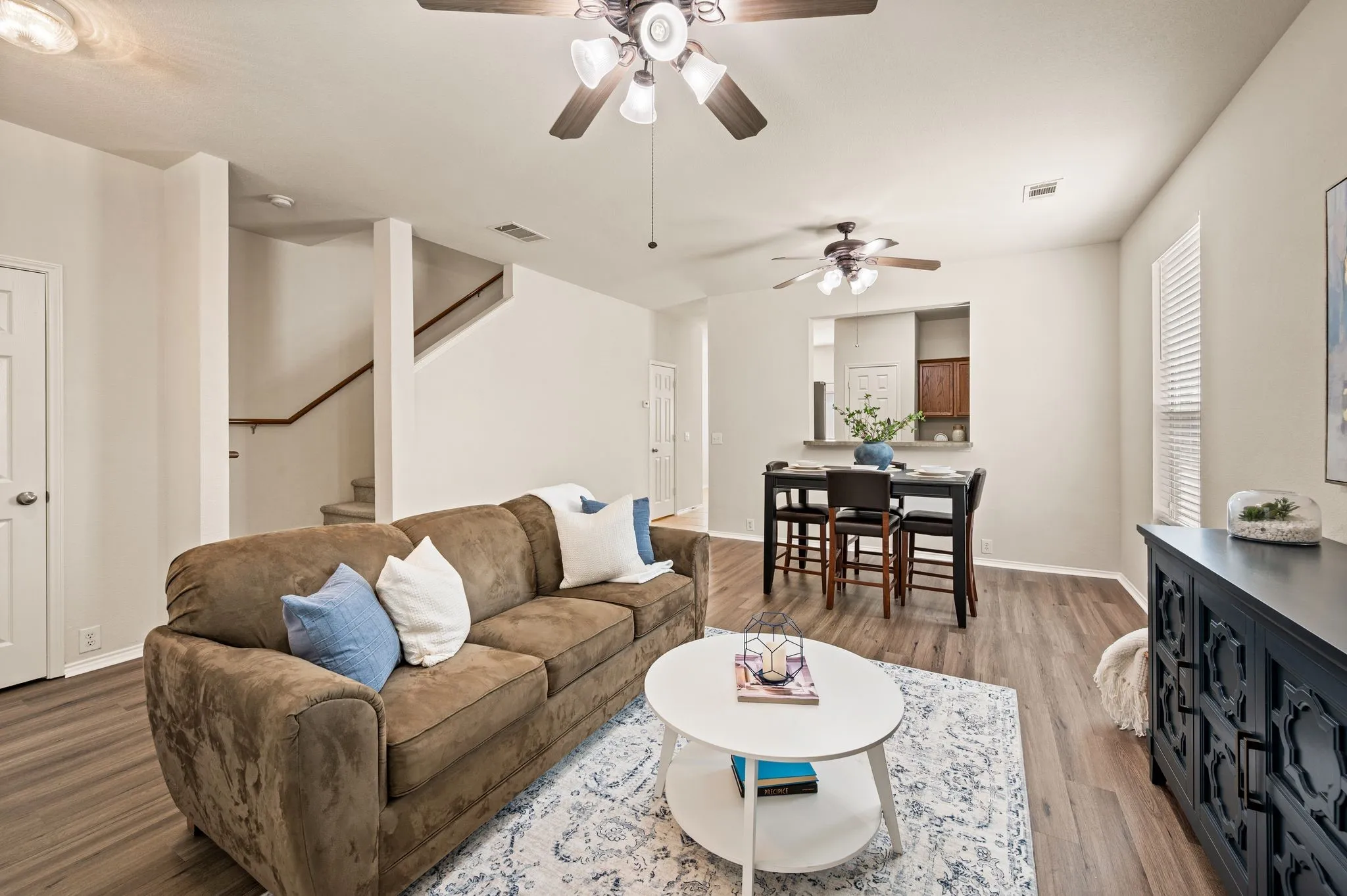 Open-concept living area with wood-finish flooring, staircase with wood handrail, and multiple ceiling fans