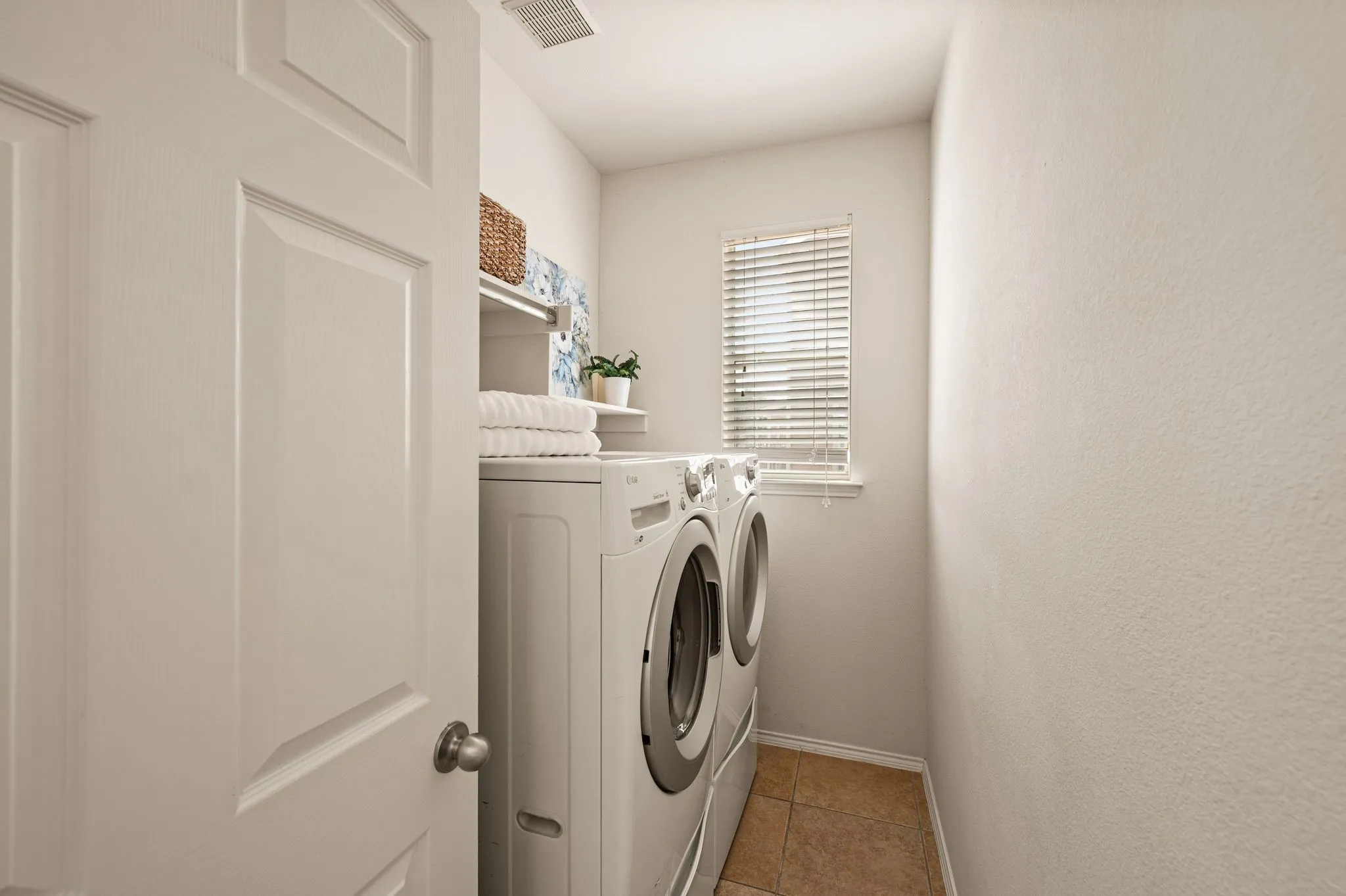 Dedicated laundry room featuring side-by-side front-load washer and dryer, ample cabinetry and countertop workspace, natural light from a louvered window, and wood-finish flooring throughout