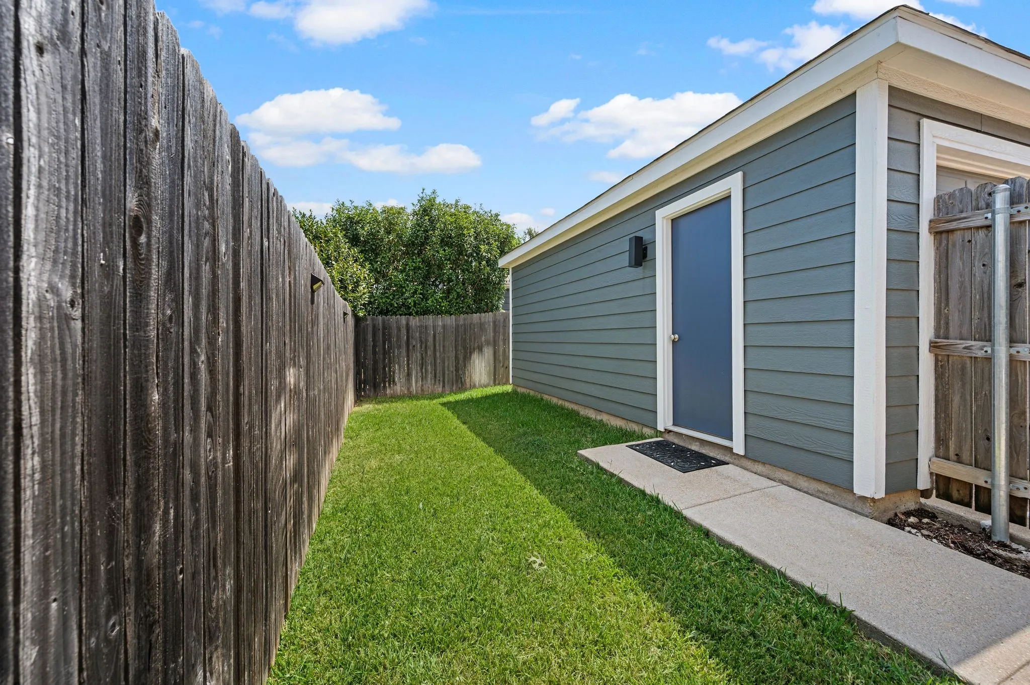 Privacy fencing enclosing a grassy side yard with a concrete pathway leading to a utility door