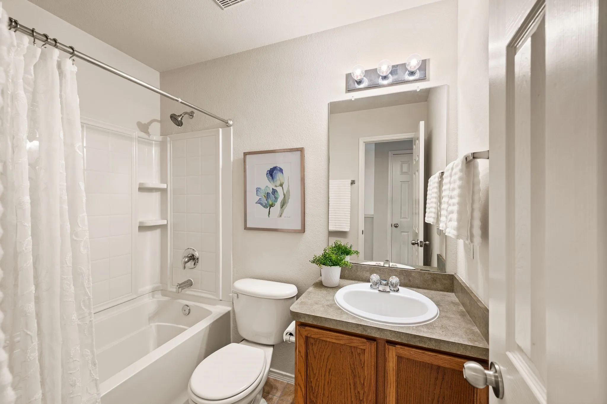 Full bathroom featuring a tub and shower combination with white tile surround, a single vanity with wood-finish cabinetry, and a chrome light fixture