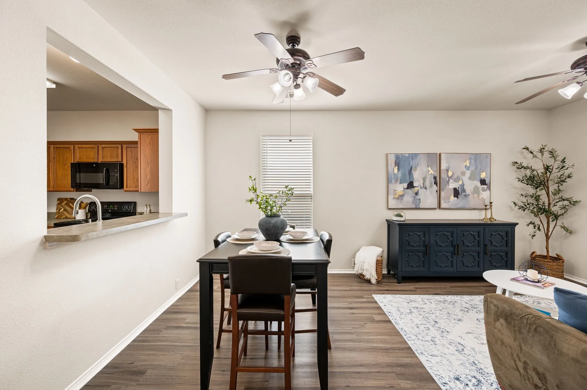 Kitchen pass-through with a stone countertop, wood-finish flooring, and two ceiling fans with integrated lighting