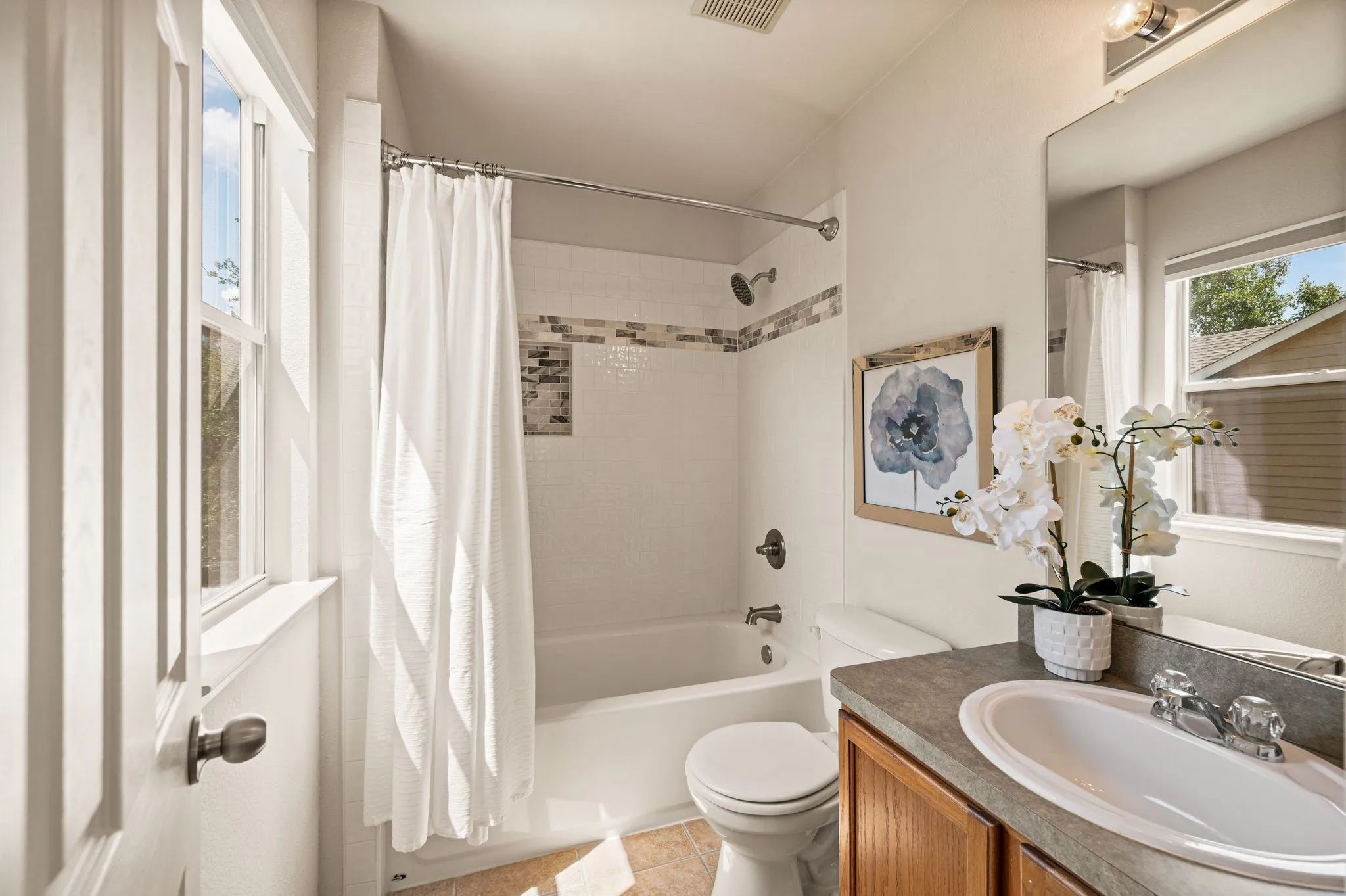 White ceramic bathtub with a shower, a vanity featuring a single basin sink, a toilet, and a window with white trim
