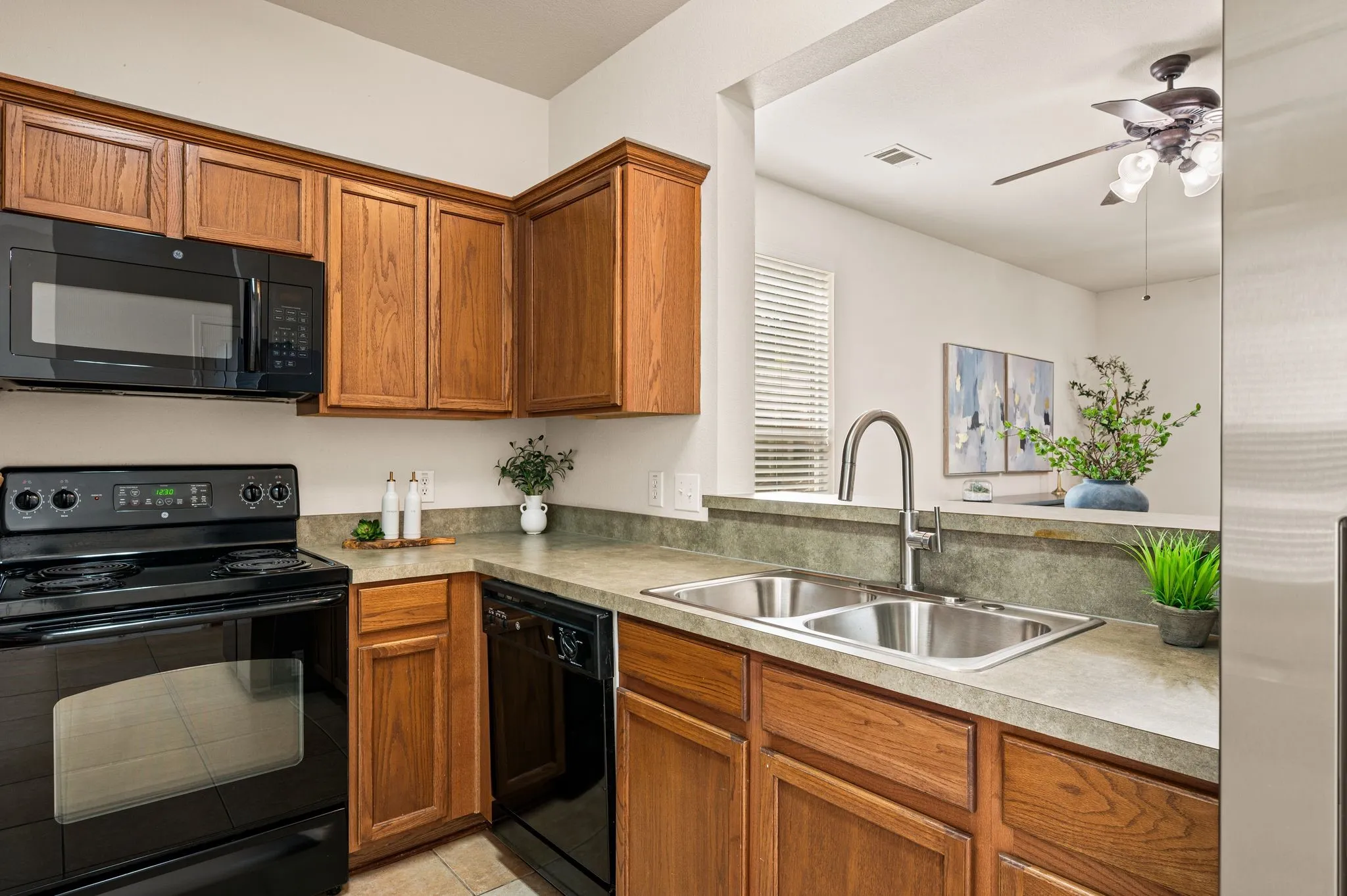 Kitchen featuring wood-finish cabinetry, black appliances, a double basin stainless steel sink, and a gooseneck faucet