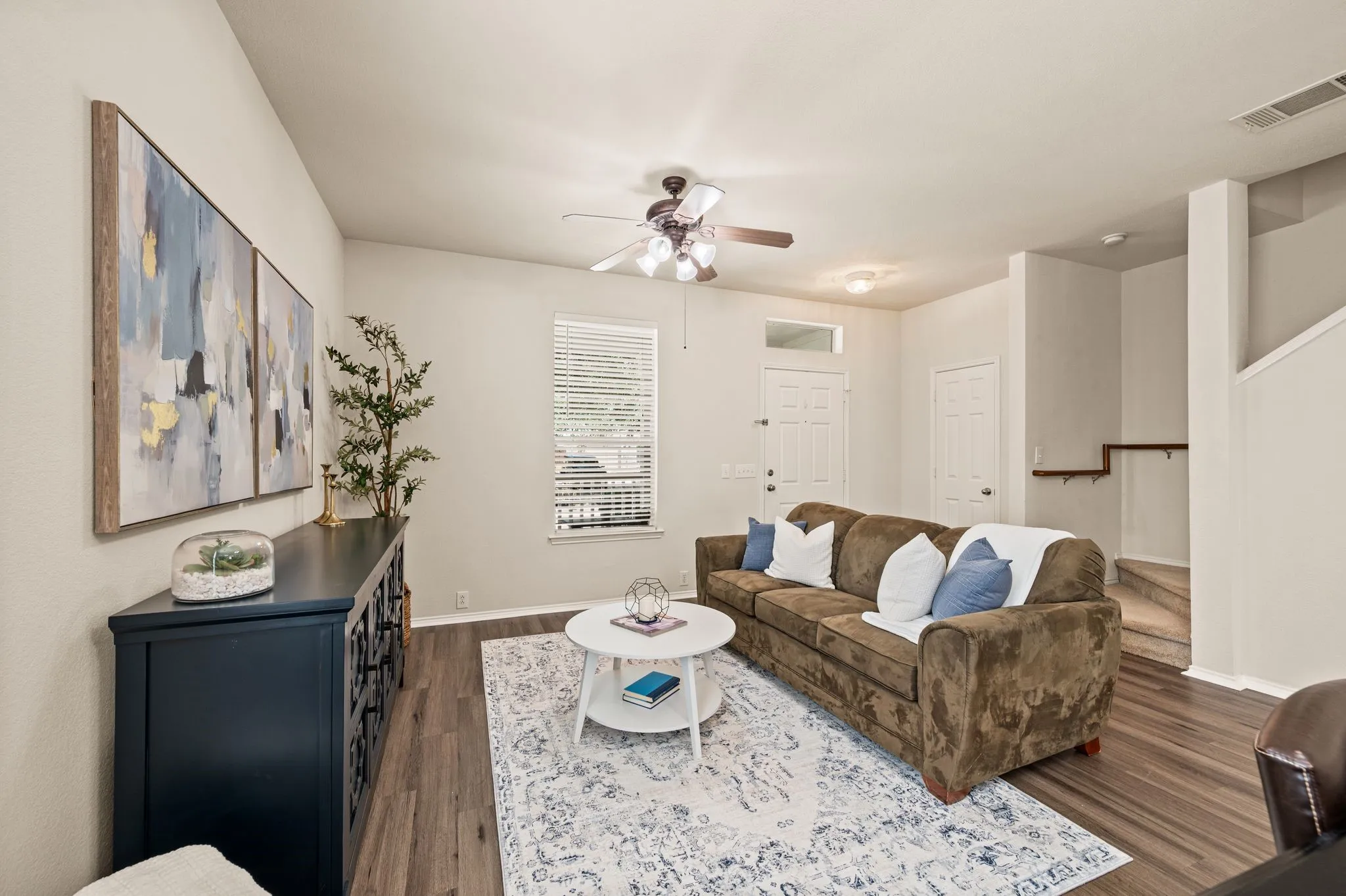 Spacious living area featuring wood-finish flooring, a ceiling fan, and window blinds