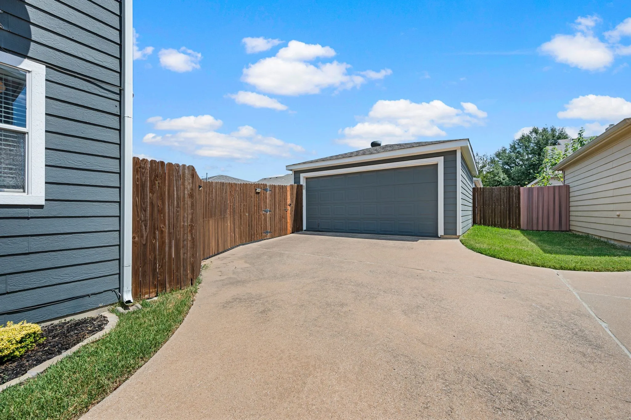 Detached garage structure with a concrete driveway, wood privacy fencing, and landscaped perimeter