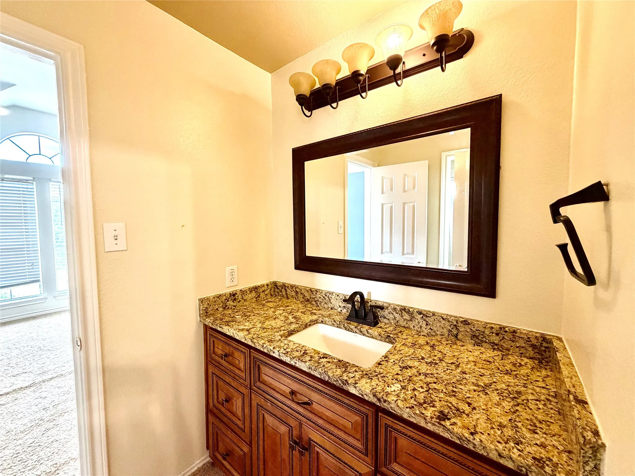 Vanity with built-in sink, dark wood-finish cabinetry, speckled countertop, and wall-mounted light fixture