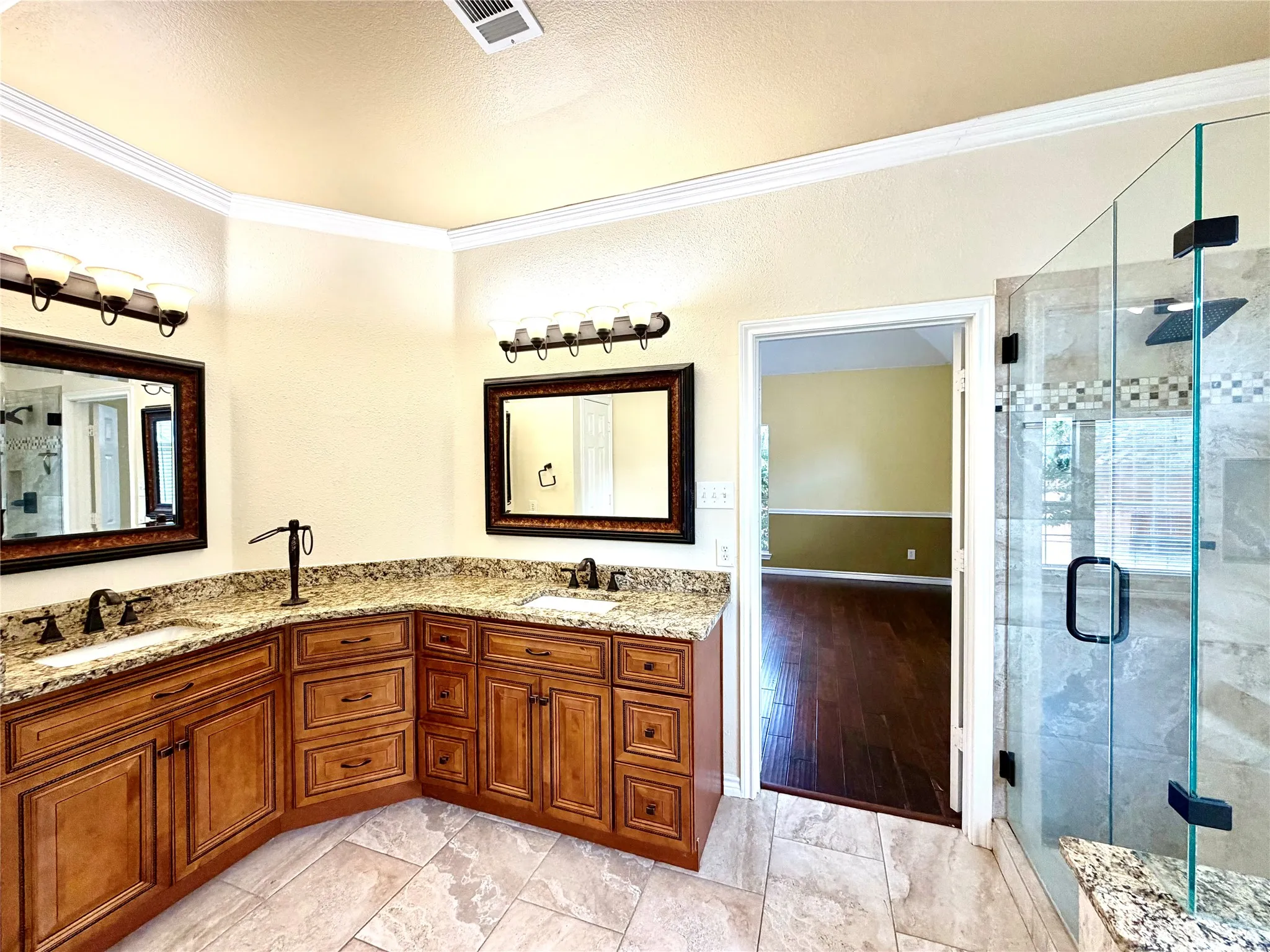 Dual vanity with granite countertops, custom wood cabinetry, tiled flooring, and an enclosed glass shower