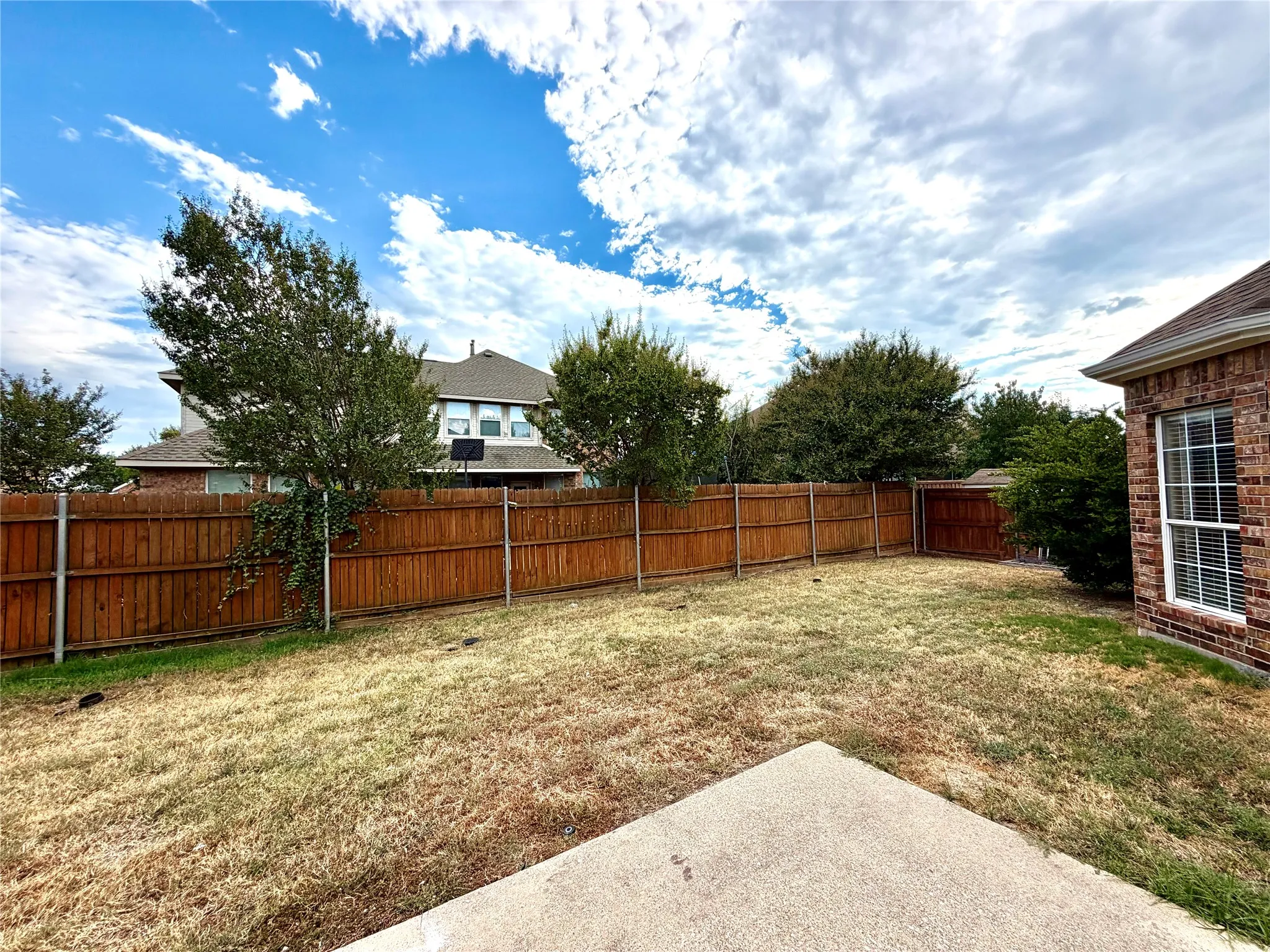 Expansive backyard featuring a wood privacy fence, concrete patio, and mature trees