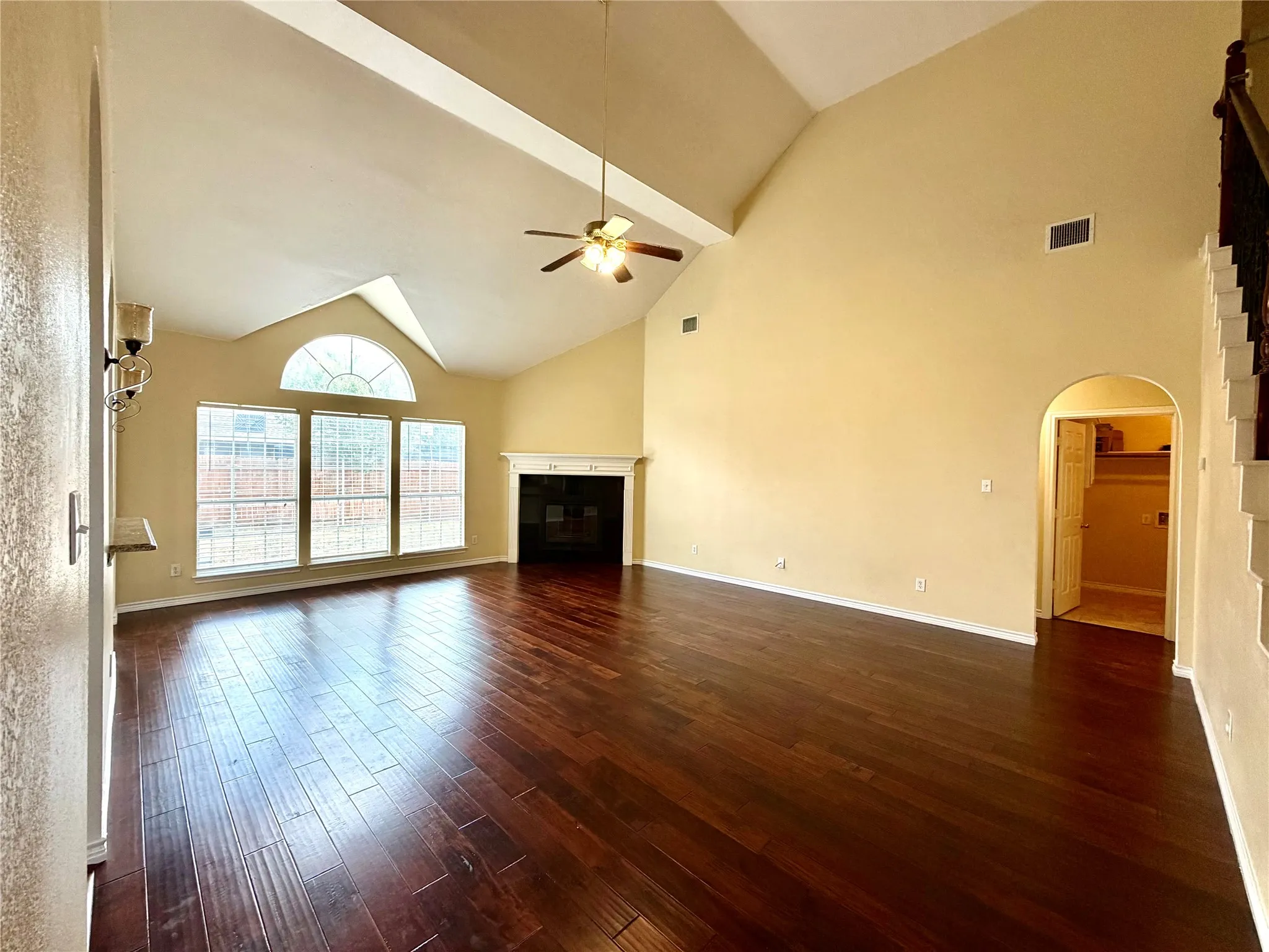 Vaulted ceiling, ceiling fan, fireplace with mantel, dark wood-finish flooring, and arched entryway