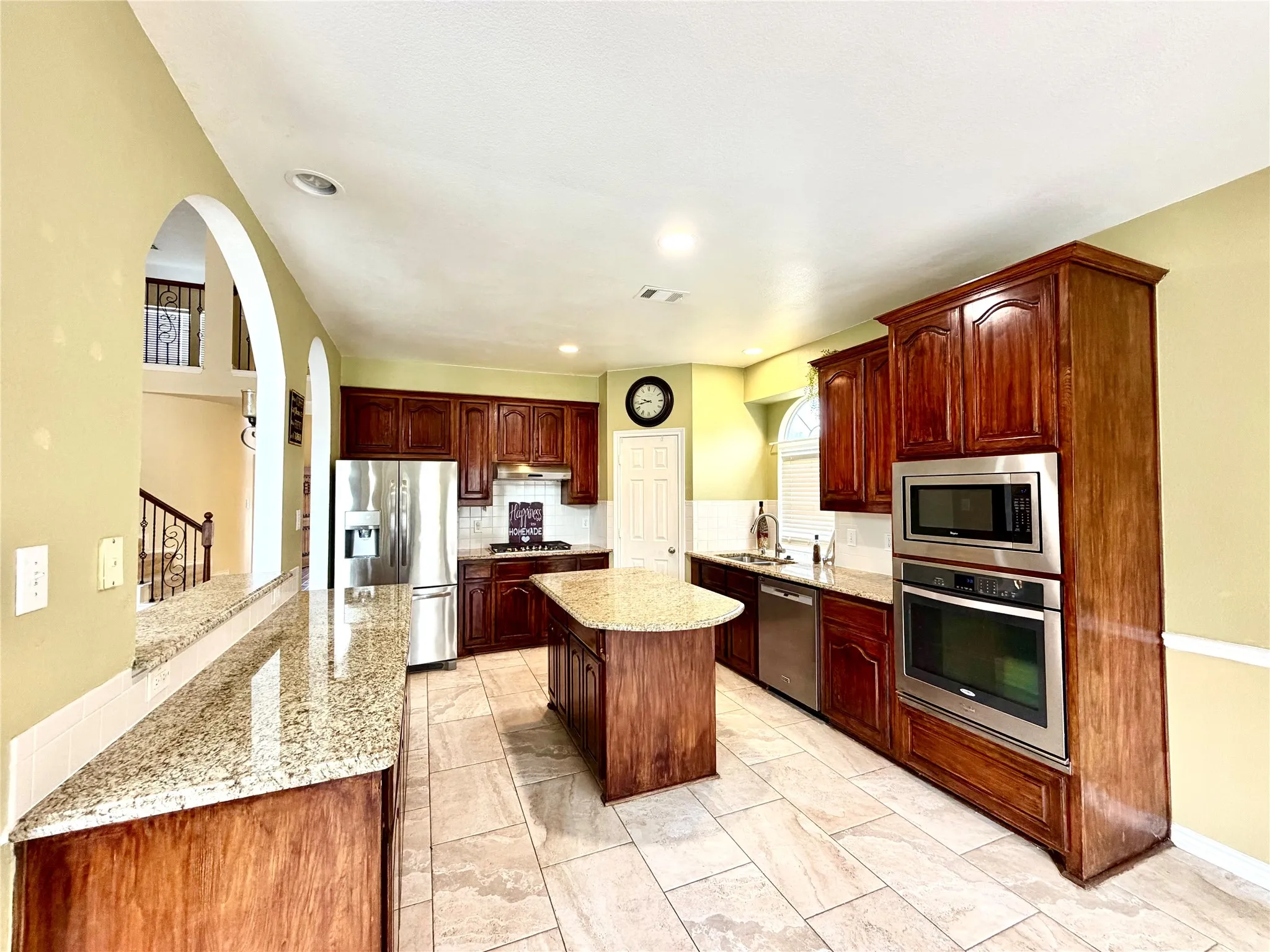 Kitchen featuring wood cabinetry, stainless steel appliances, granite countertops, a central island, and tile flooring
